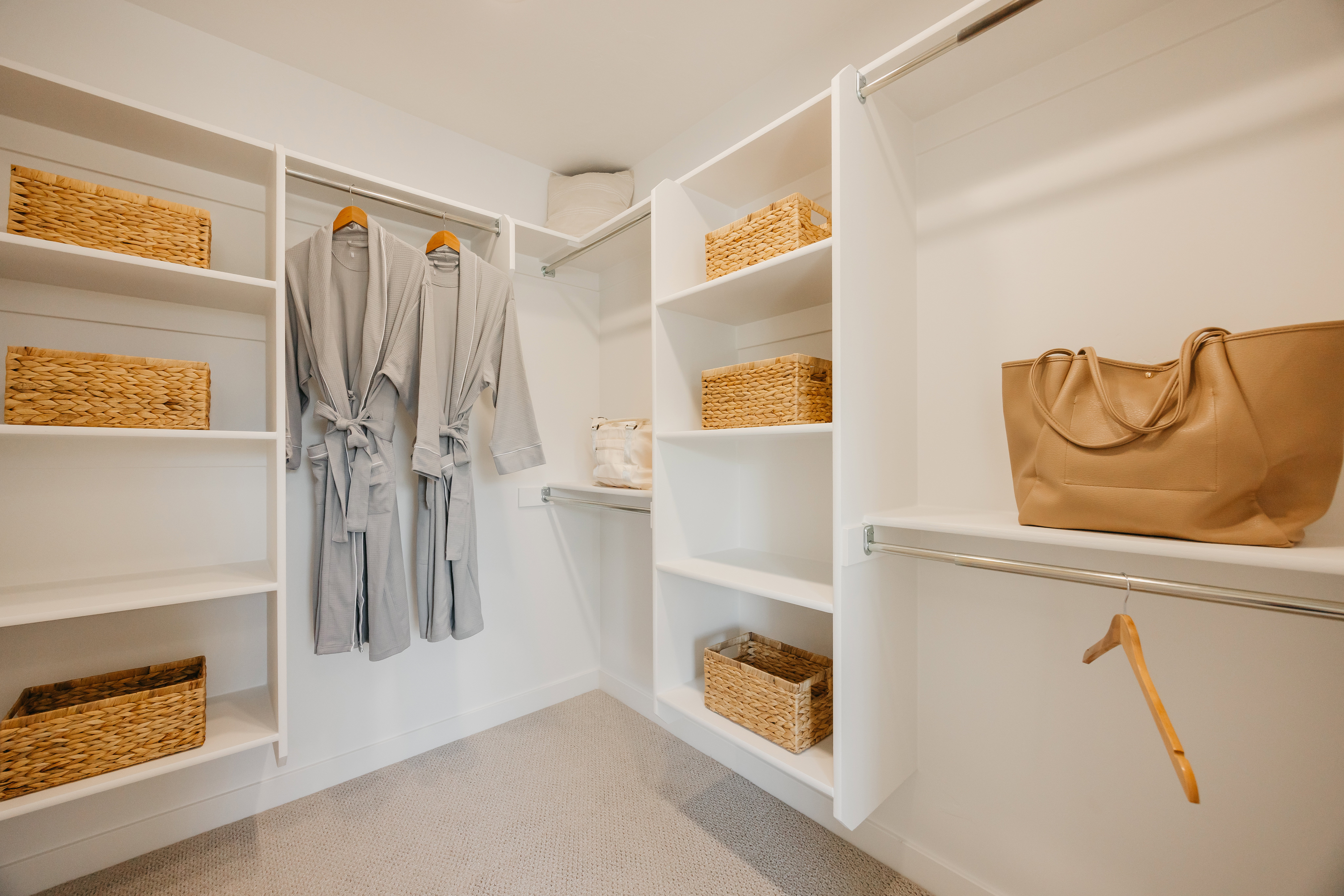 Custom closet system featuring white shelving, multiple hanging rods, and light-colored carpet flooring