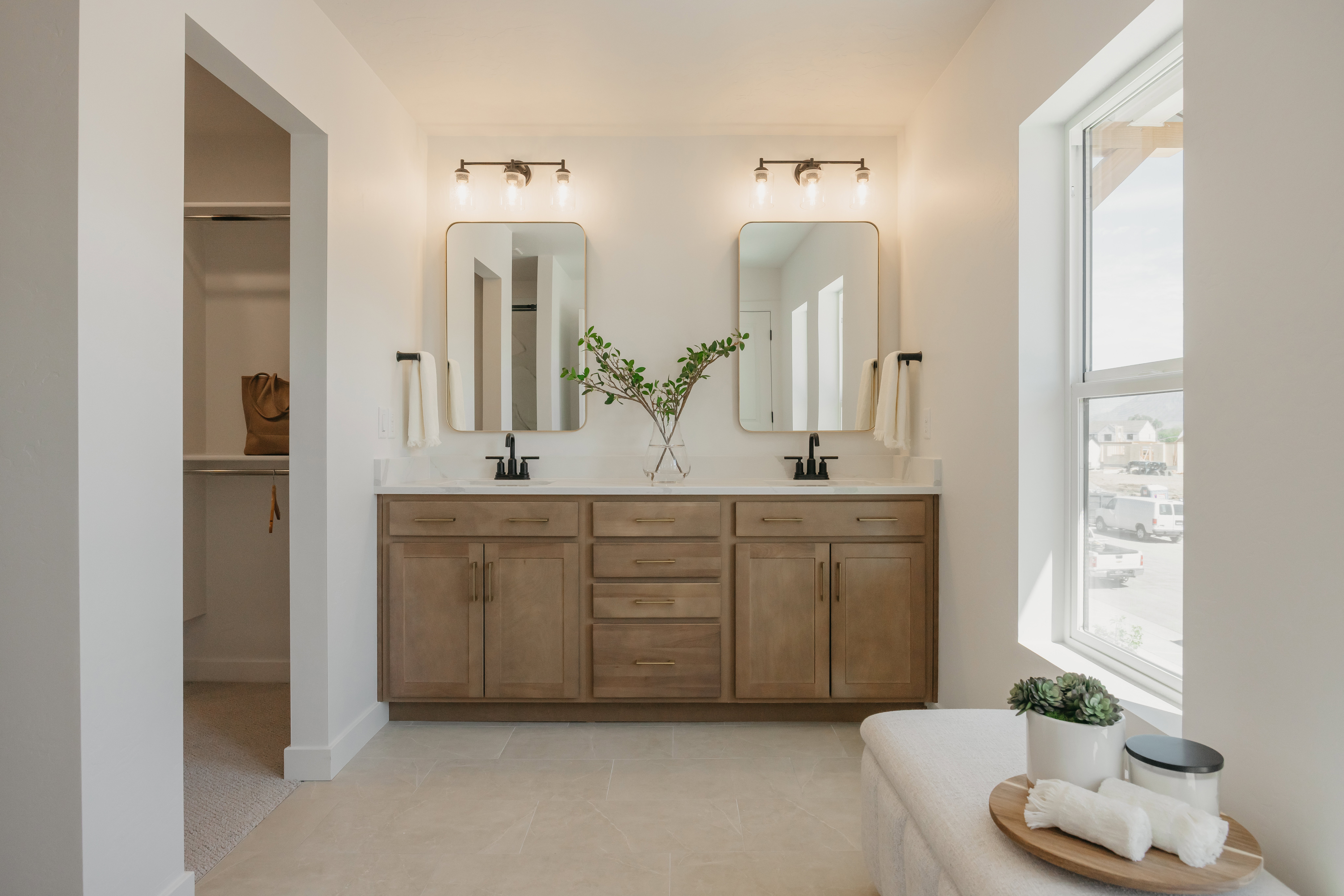 Dual vanity featuring neutral-toned wood cabinetry with matte black hardware, under-mount sinks, and light-toned countertops