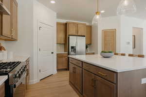Kitchen featuring a spacious island with seating, stainless steel appliances, wood-finish flooring, recessed lighting, and warm-toned cabinetry with brass hardware