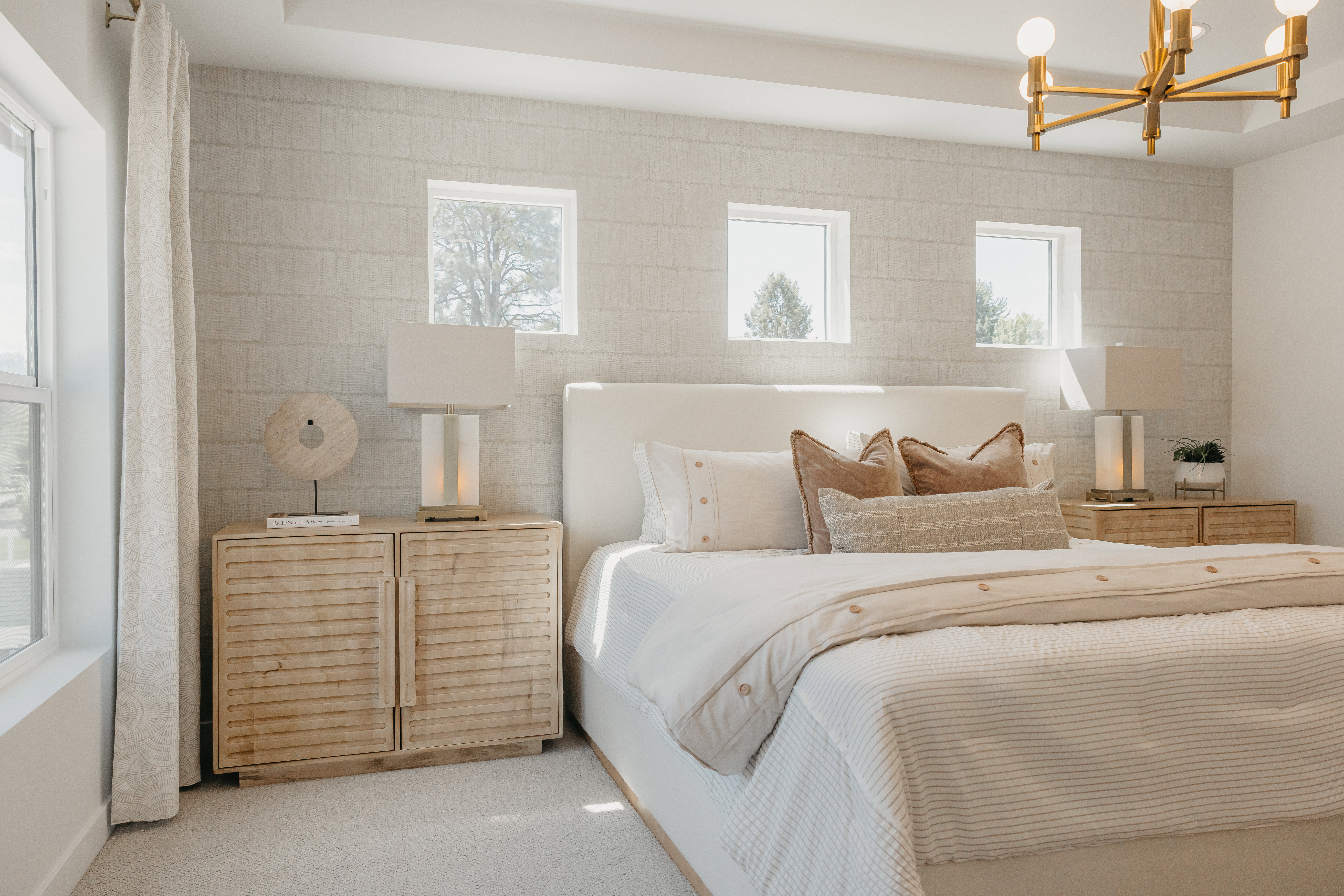 Spacious bedroom featuring textured wall treatment, recessed ceiling detail, and a modern brass chandelier