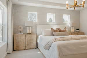 Spacious bedroom featuring textured wall treatment, recessed ceiling detail, and a modern brass chandelier