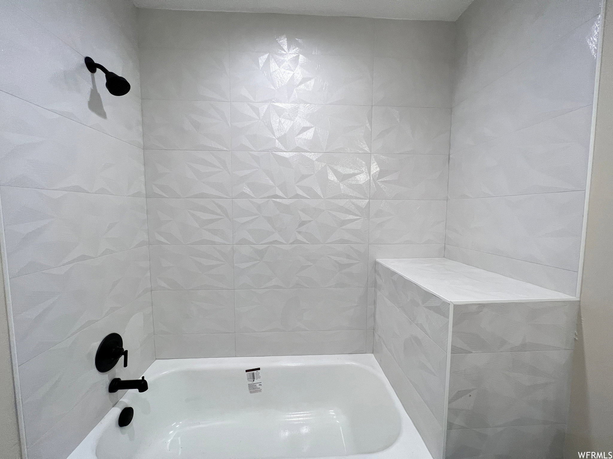 Bathtub and shower combination featuring geometric pattern wall tile, a built-in shower bench, and matte black fixtures
