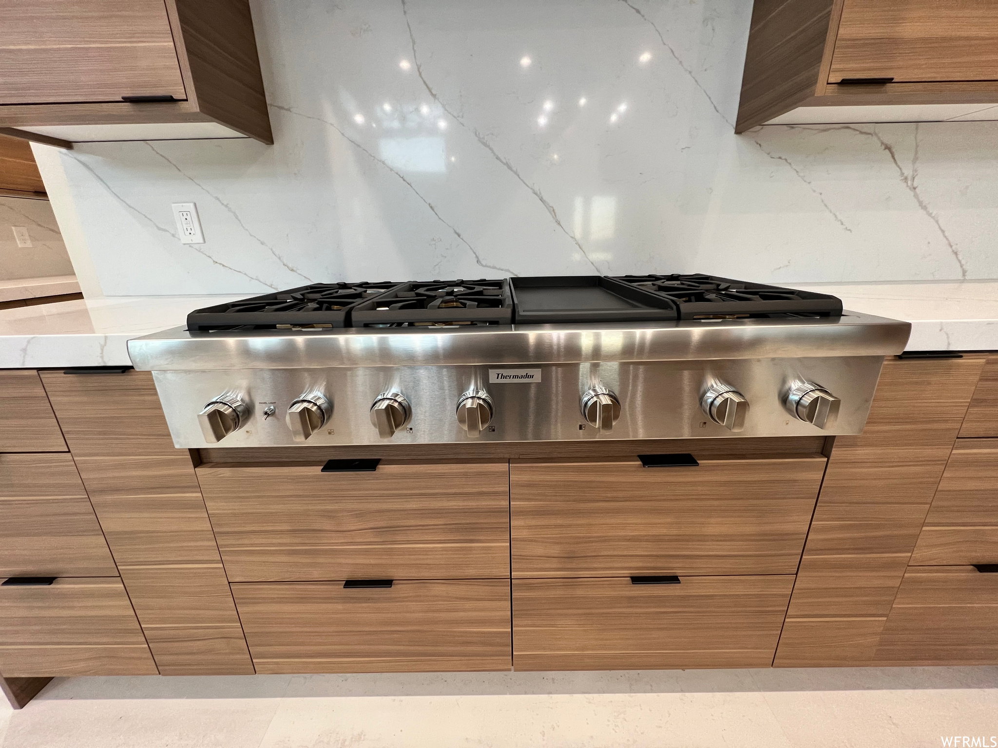 Stainless steel gas range with a griddle, set into white stone countertops and a matching stone backsplash