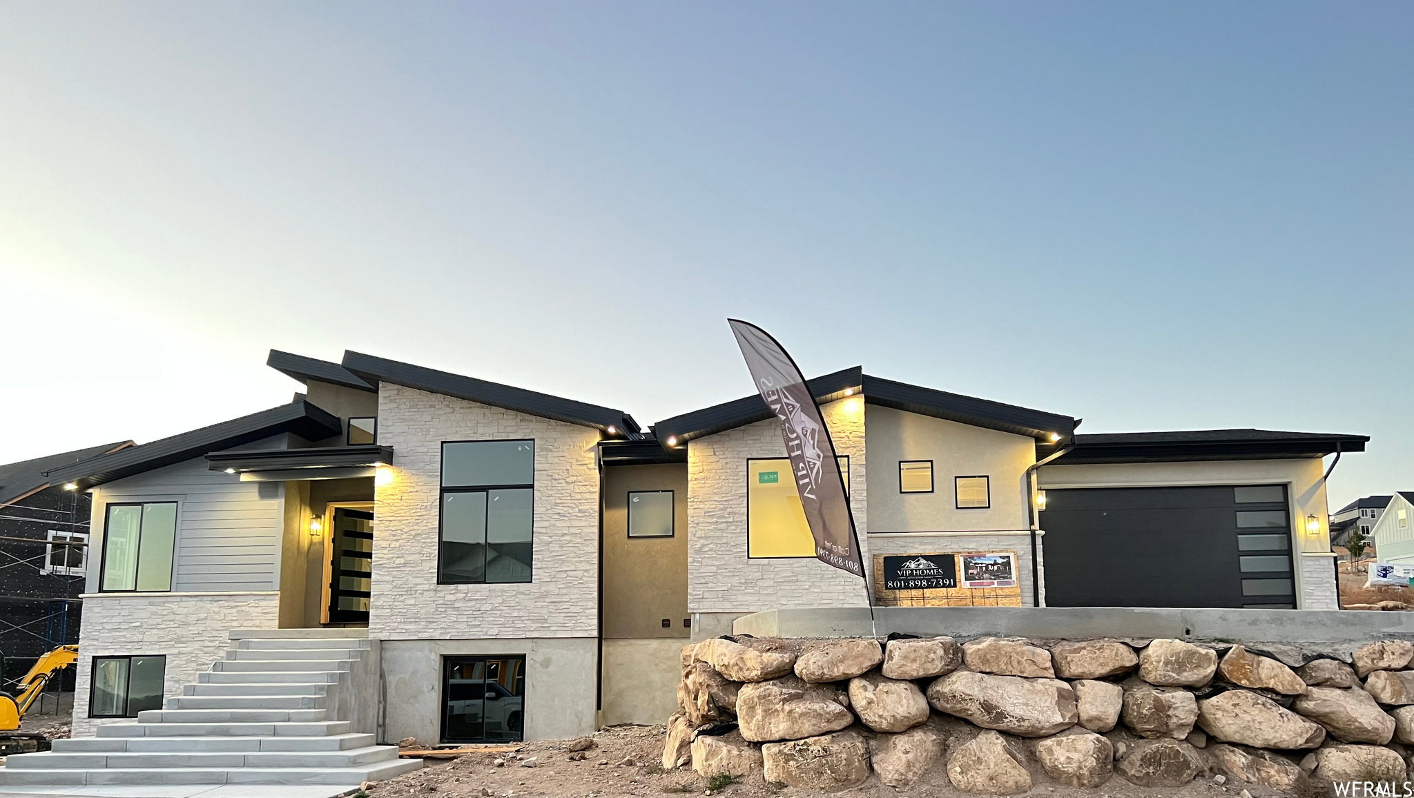 Modern exterior featuring multi-textured facade, stone accents, a prominent front entry with a full-view door, a contemporary garage door, and stepped concrete pathways