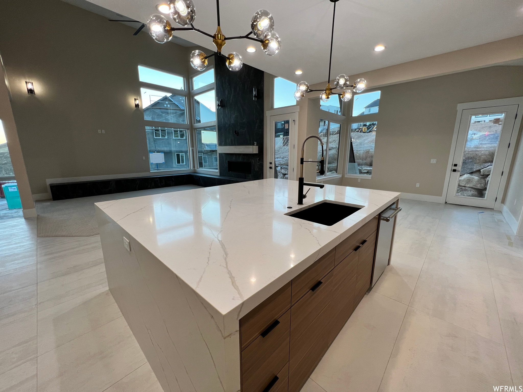 Kitchen island featuring a white countertop with veining, an undermount sink with a matte black faucet, and wood-finish cabinetry with black hardware