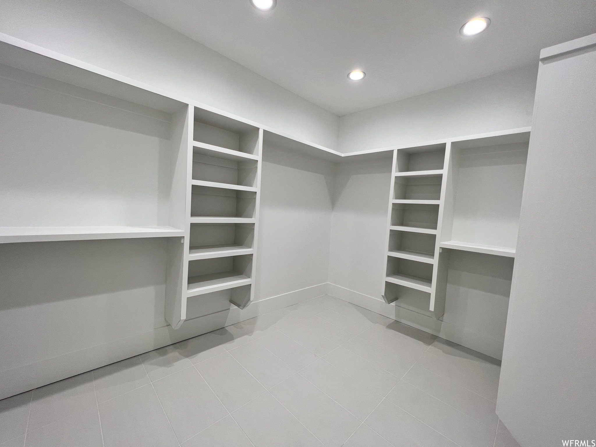 Spacious walk-in closet featuring extensive built-in shelving, integrated storage compartments, recessed ceiling lighting, and light-toned tile flooring