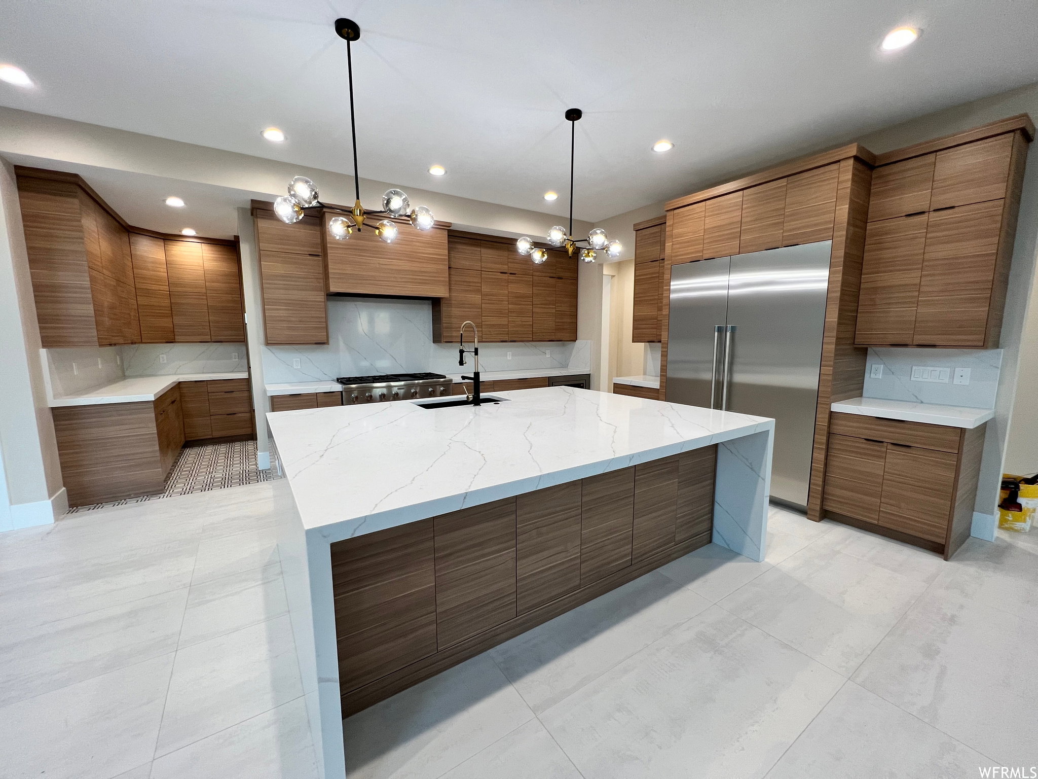 Modern kitchen featuring a large waterfall island with a quartz countertop, wood-finish cabinetry, stainless steel refrigerator, gas range, and geometric pendant lighting fixtures
