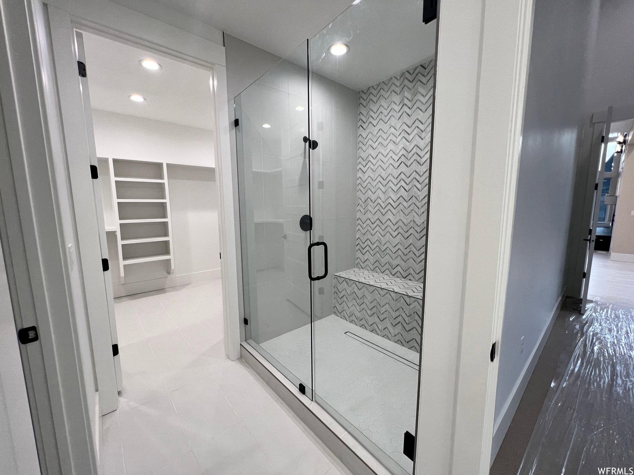 Glass-enclosed shower featuring a tiled bench, matte black fixtures, and chevron-patterned accent tiling