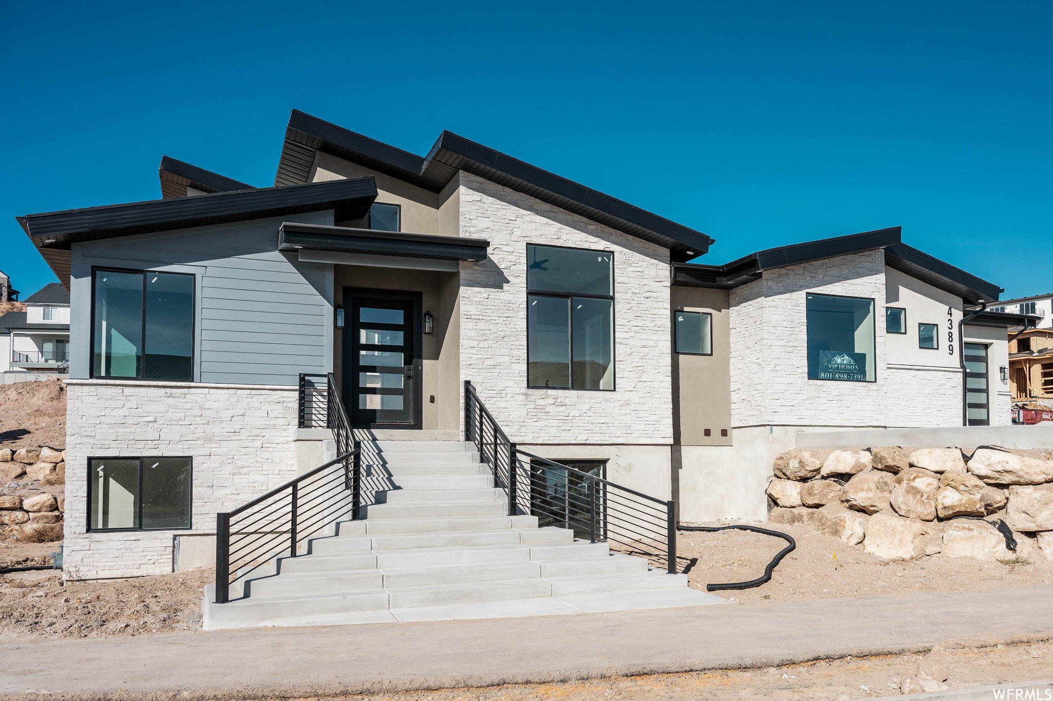 Modern architectural exterior with an angled roofline, stone veneer, horizontal siding accents, multiple large windows, and a contemporary entry door with glass panels