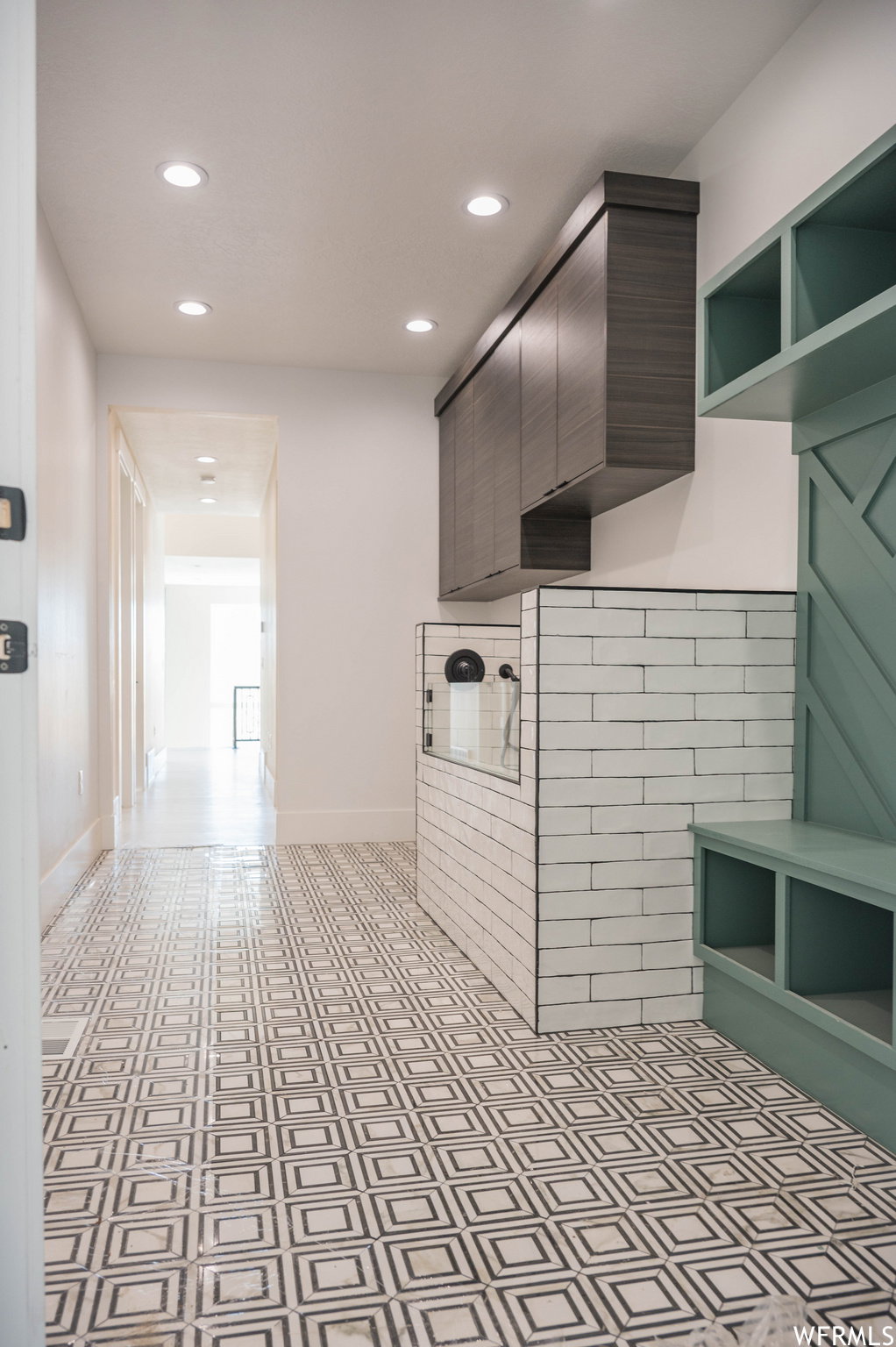 Geometric pattern tile flooring, recessed ceiling lighting, built-in shelving, dark wood-finish cabinetry, and white subway tile surround