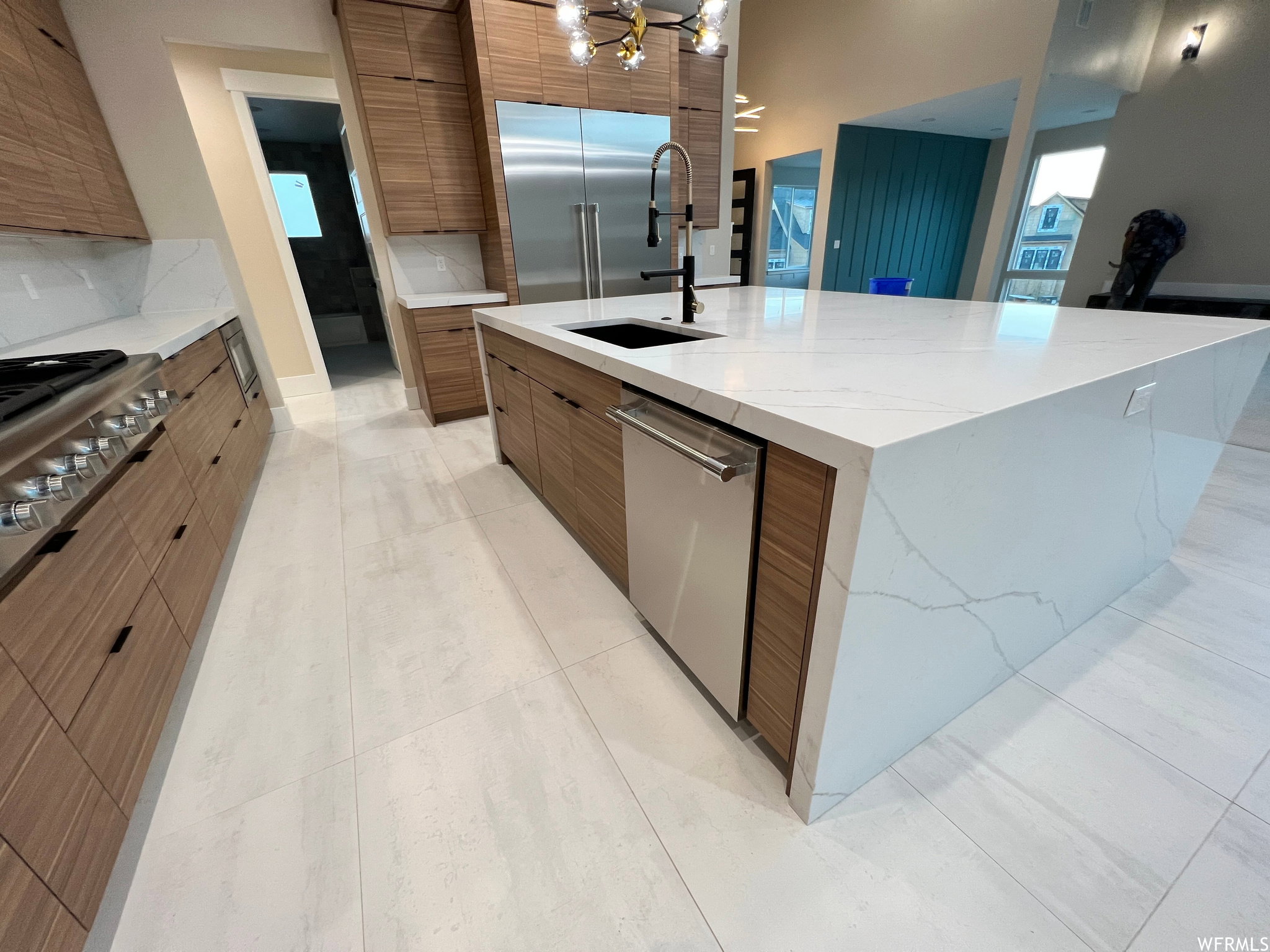 Kitchen featuring a waterfall island with integrated sink, stainless steel appliances, wood-finish cabinetry, white countertops, and light-toned tile flooring