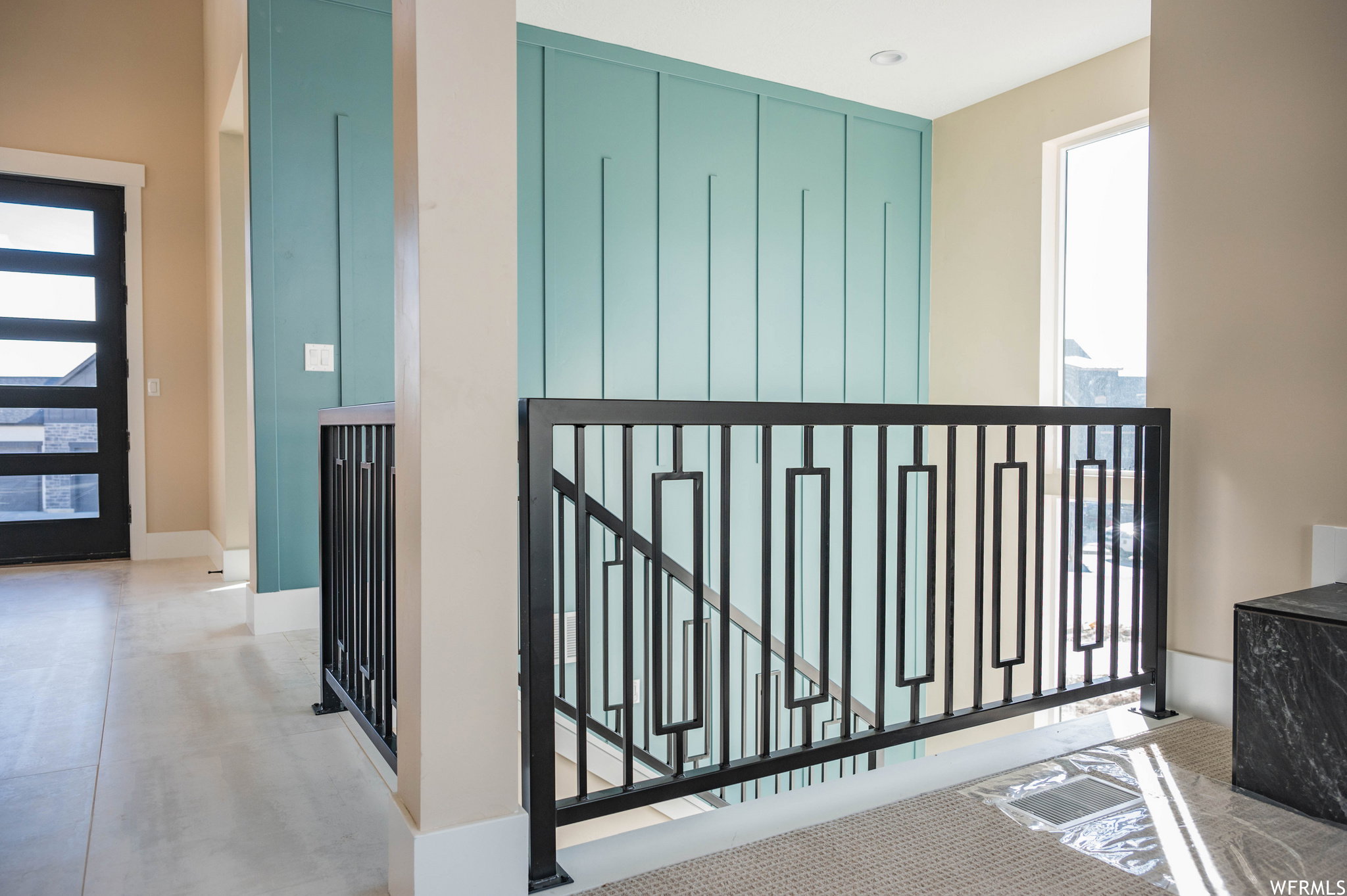 Entryway featuring a modern black glass-paneled door, light tile flooring, and a decorative accent wall