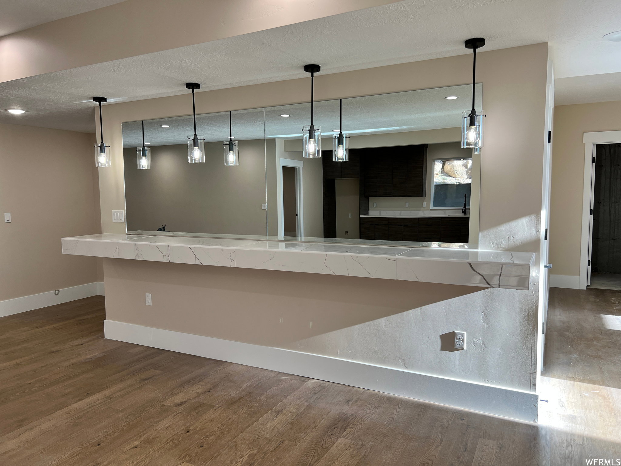 Breakfast bar featuring a waterfall-edge countertop with veining, under-counter pendant lighting, a full-height mirrored backsplash, and wood-finish flooring