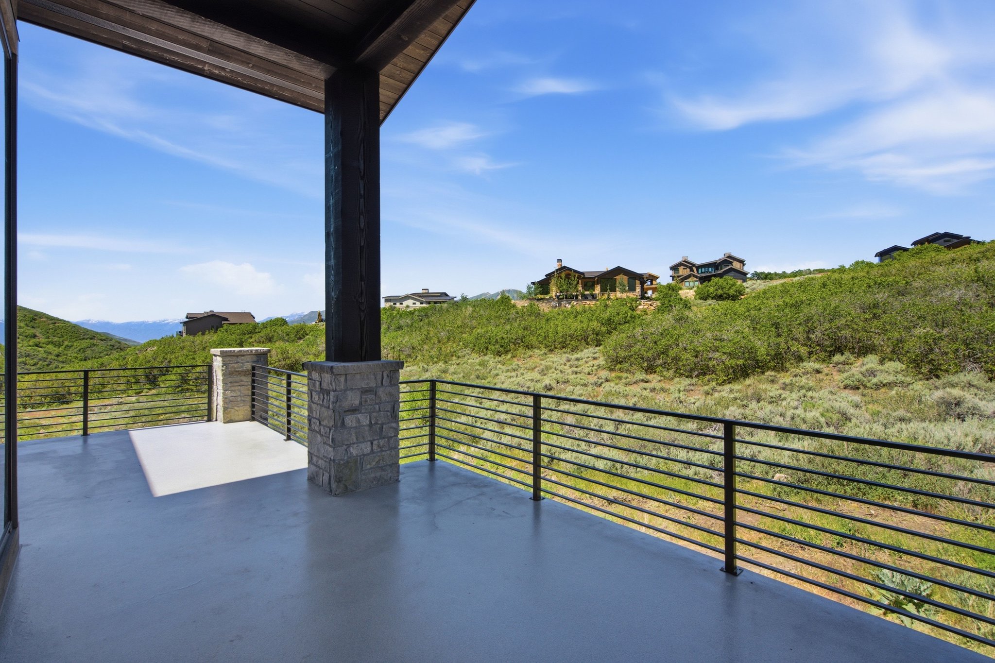 Covered outdoor deck with a smooth gray surface, featuring a horizontal bar railing system and stone-clad columns