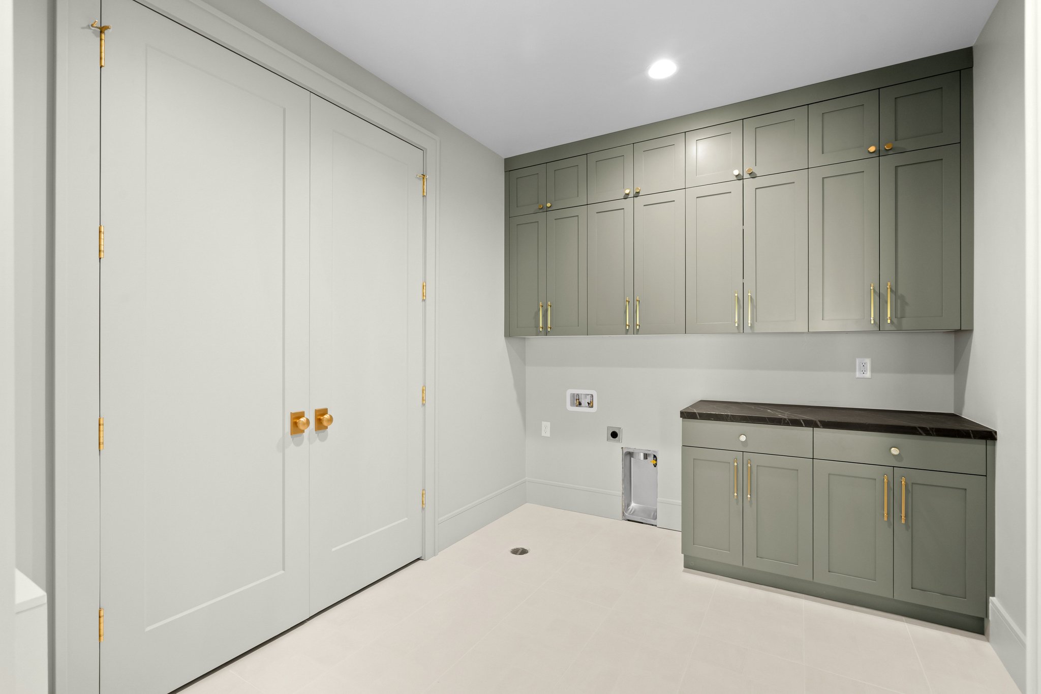 Dedicated utility room featuring extensive built-in cabinetry, elegant gold-toned hardware, a corner countertop, and durable flooring