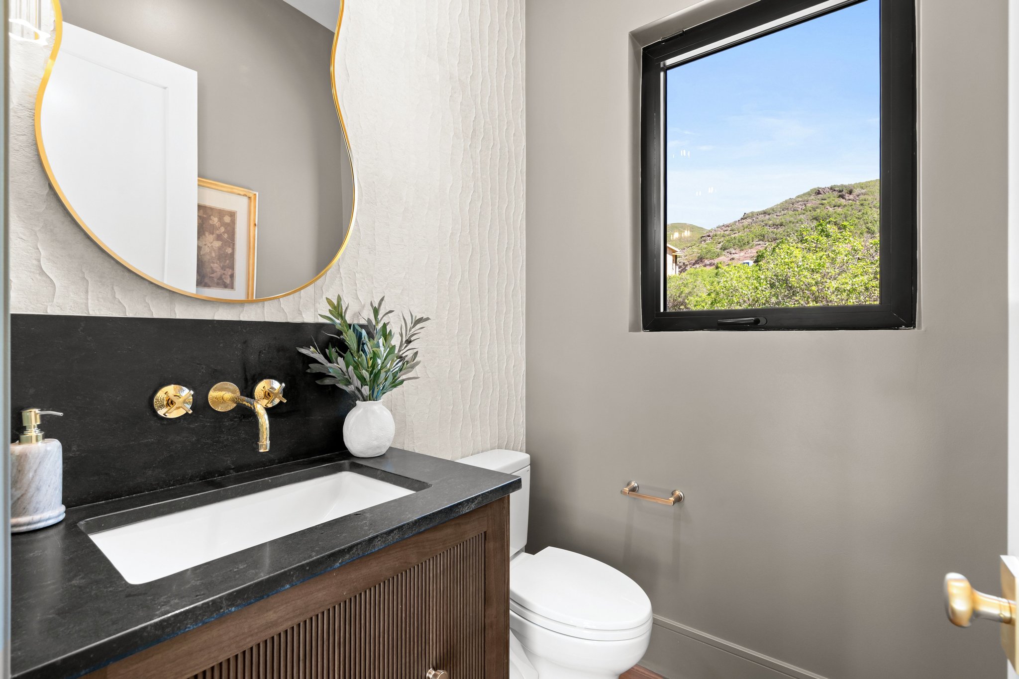 Powder room featuring a dark wood-finish vanity with fluted detailing, a dark stone countertop, and a wall-mounted brass faucet