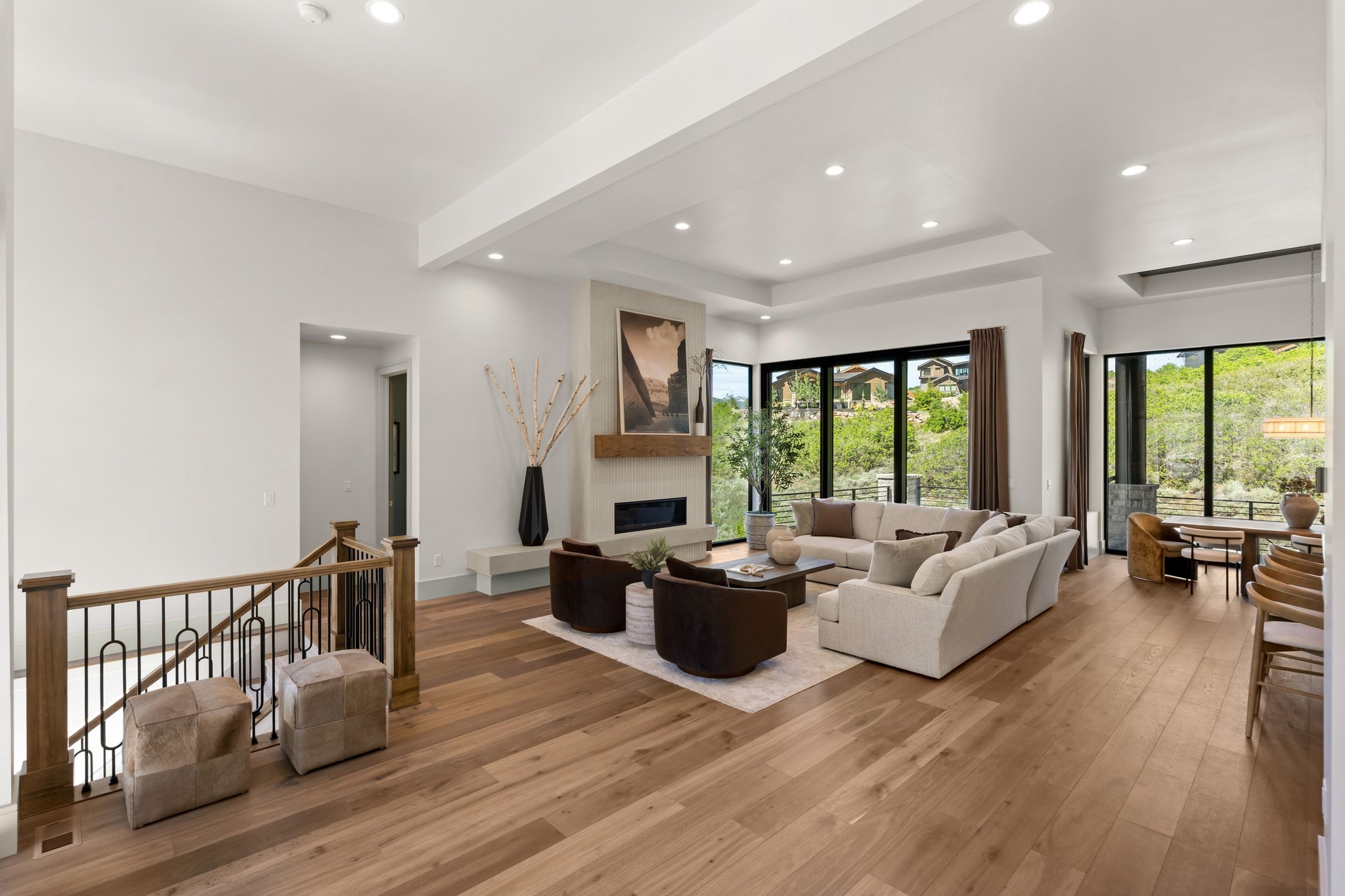 Expansive living area featuring wide plank wood-finish flooring, a contemporary fireplace with a stone surround and wood mantle, and floor-to-ceiling windows