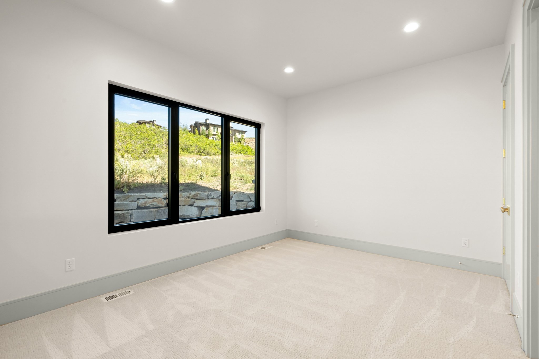 Room featuring a three-panel window with black frames, recessed ceiling lighting, light-colored carpeting, white walls, and gray baseboards