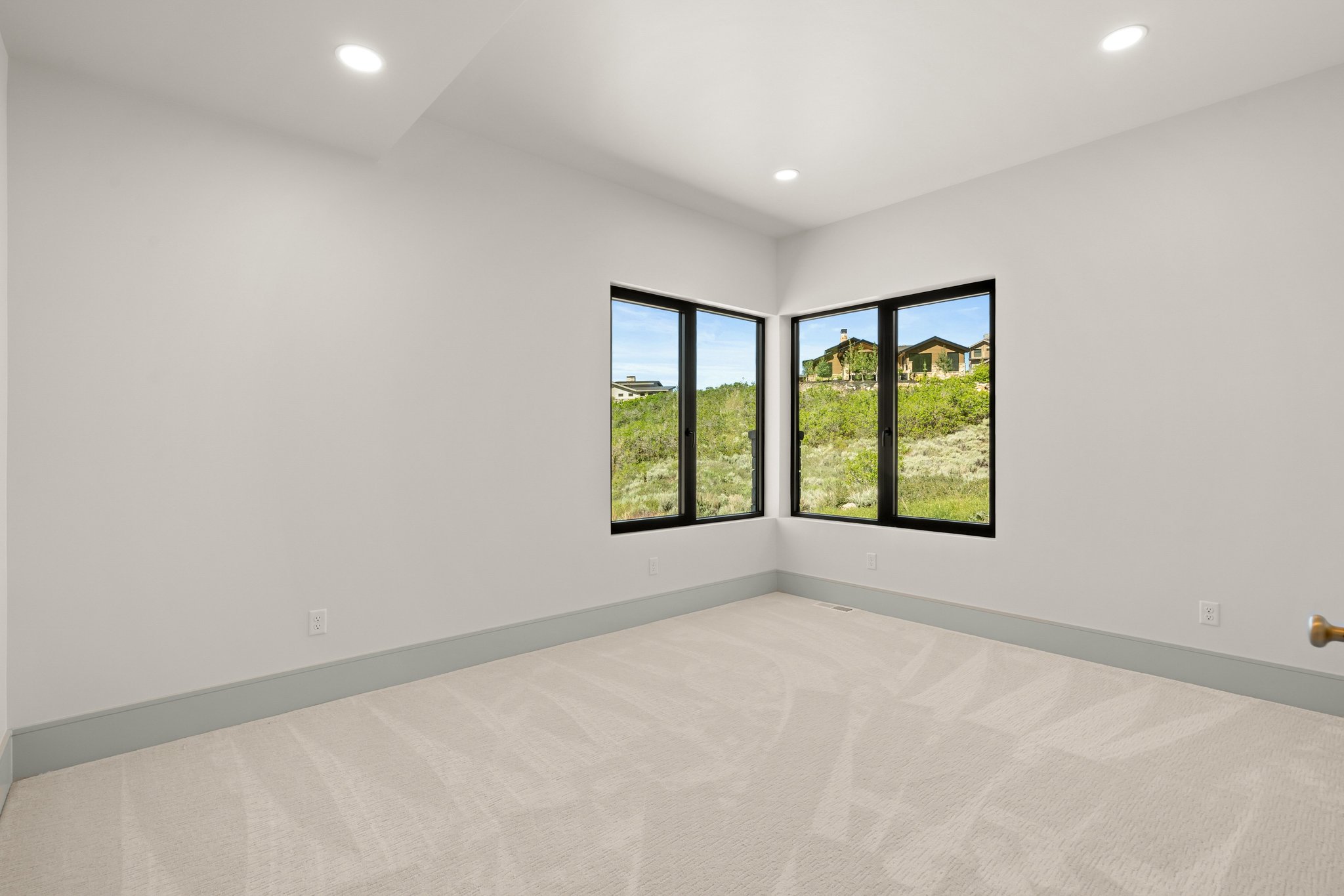 Room featuring corner windows with black frames, recessed lighting, neutral carpeting, and light gray baseboards