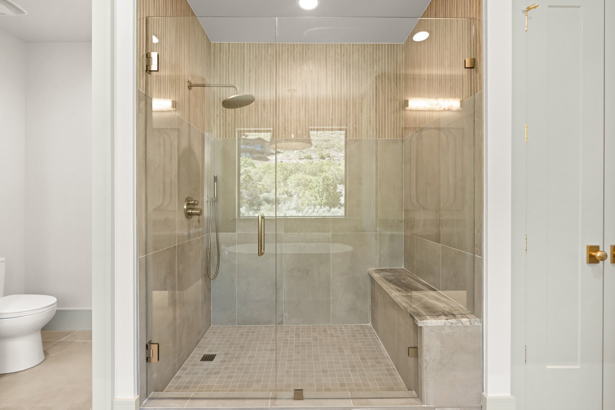 Glass-enclosed shower with a rainfall showerhead, handheld sprayer, integrated bench, and mosaic tile flooring