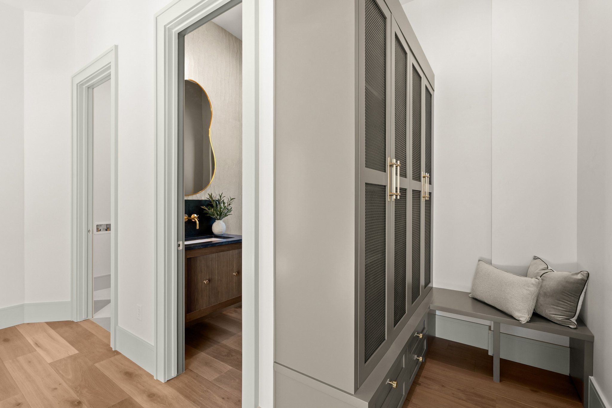 Hallway featuring wood-finish flooring, a built-in storage cabinet with metal mesh doors and brass hardware, and a built-in bench