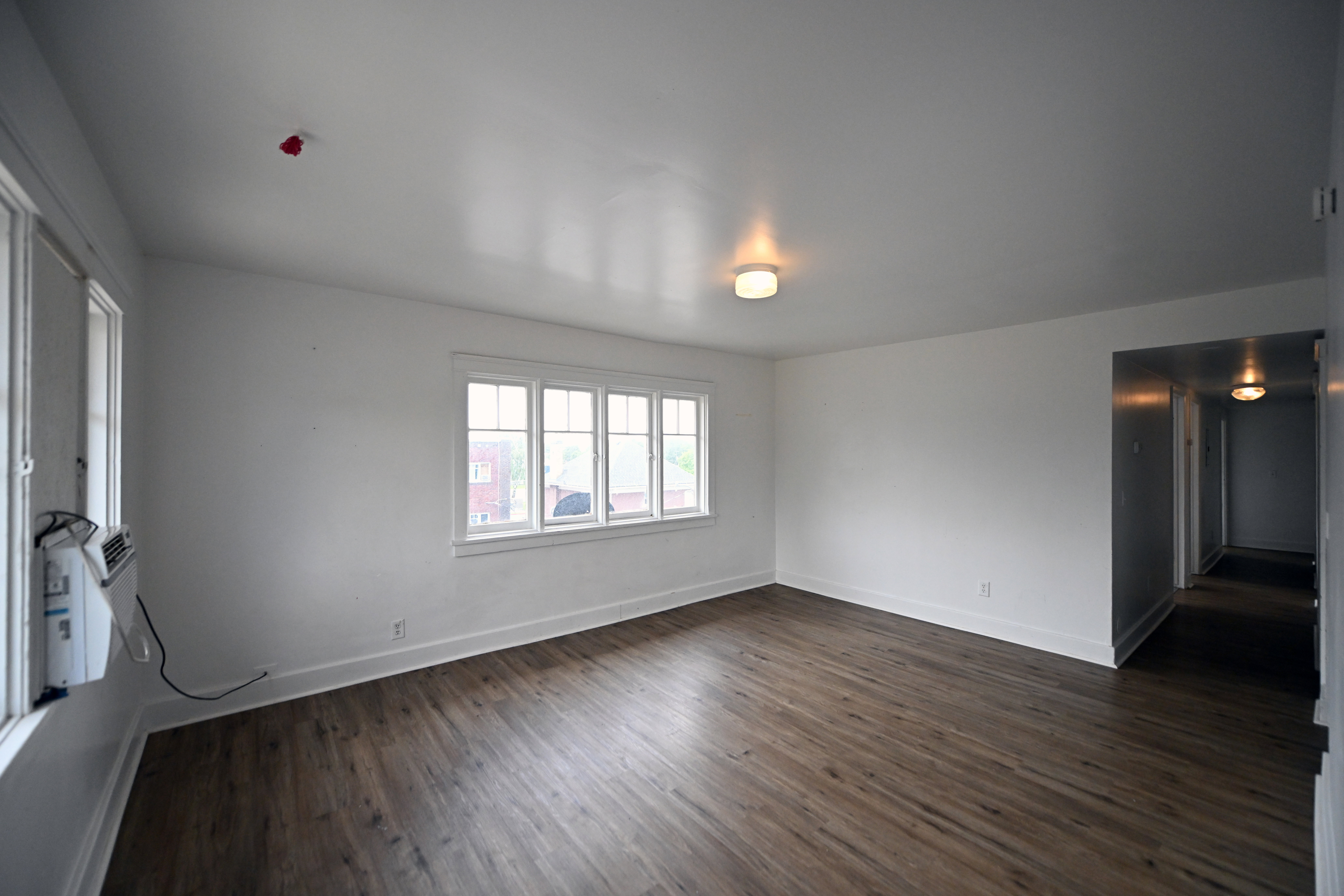 Spacious room featuring wood-finish flooring, white walls, and multiple windows allowing natural light