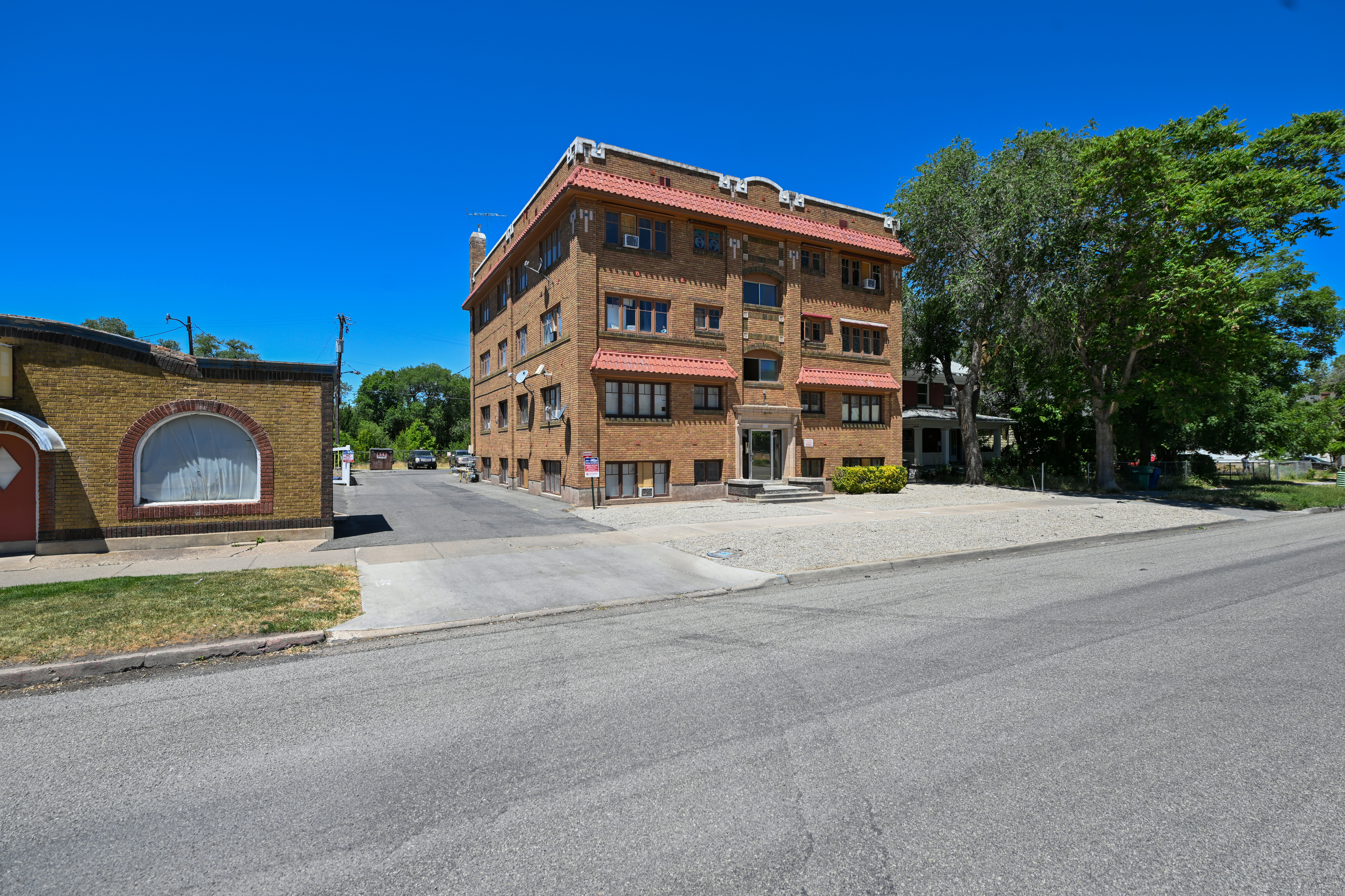 Four-story brick building featuring multiple window units, red tile roof accents, and a central entrance