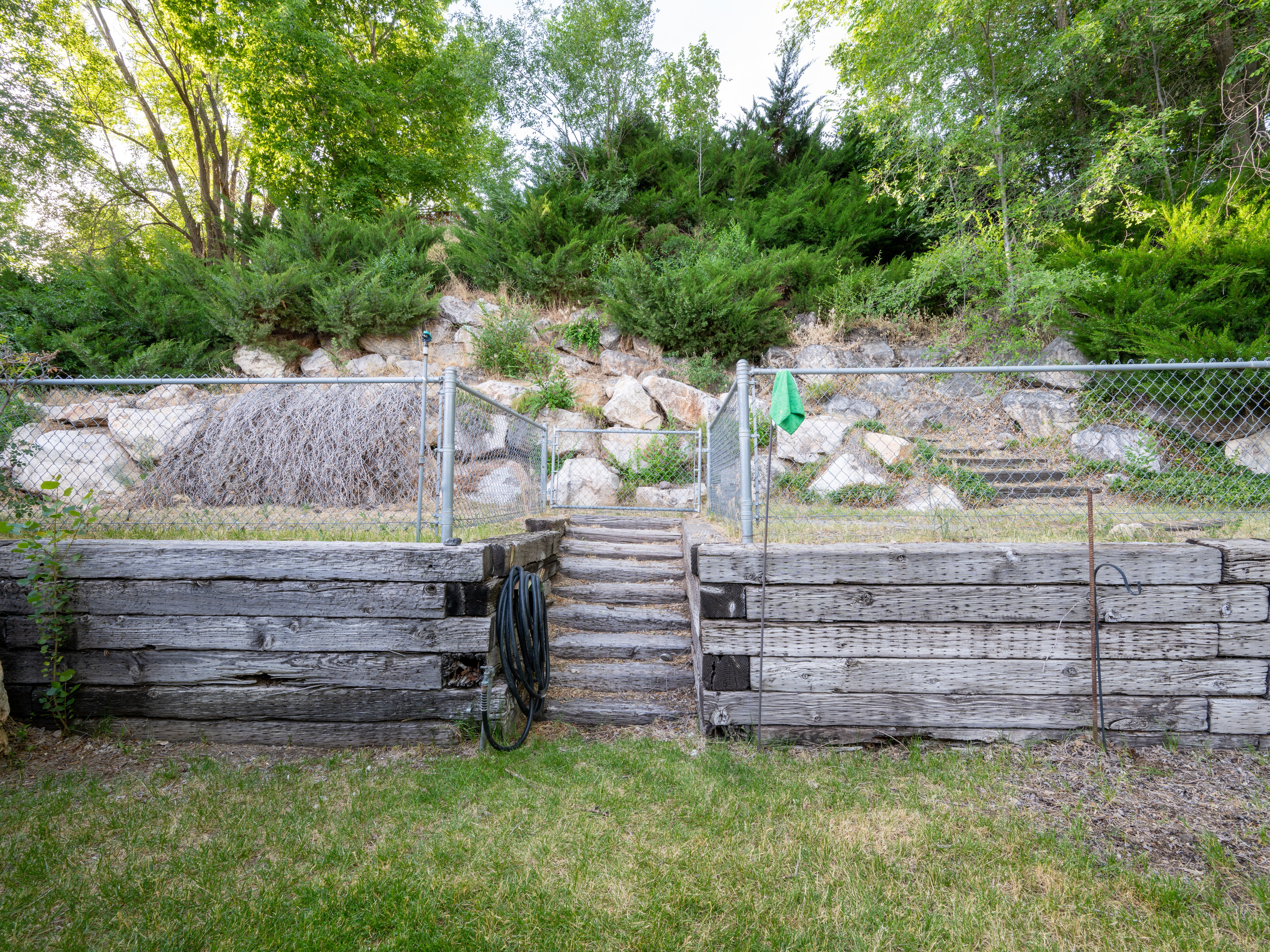 Terraced backyard featuring wood-finish retaining walls, a chain-link fence, and stone steps leading to an upper level