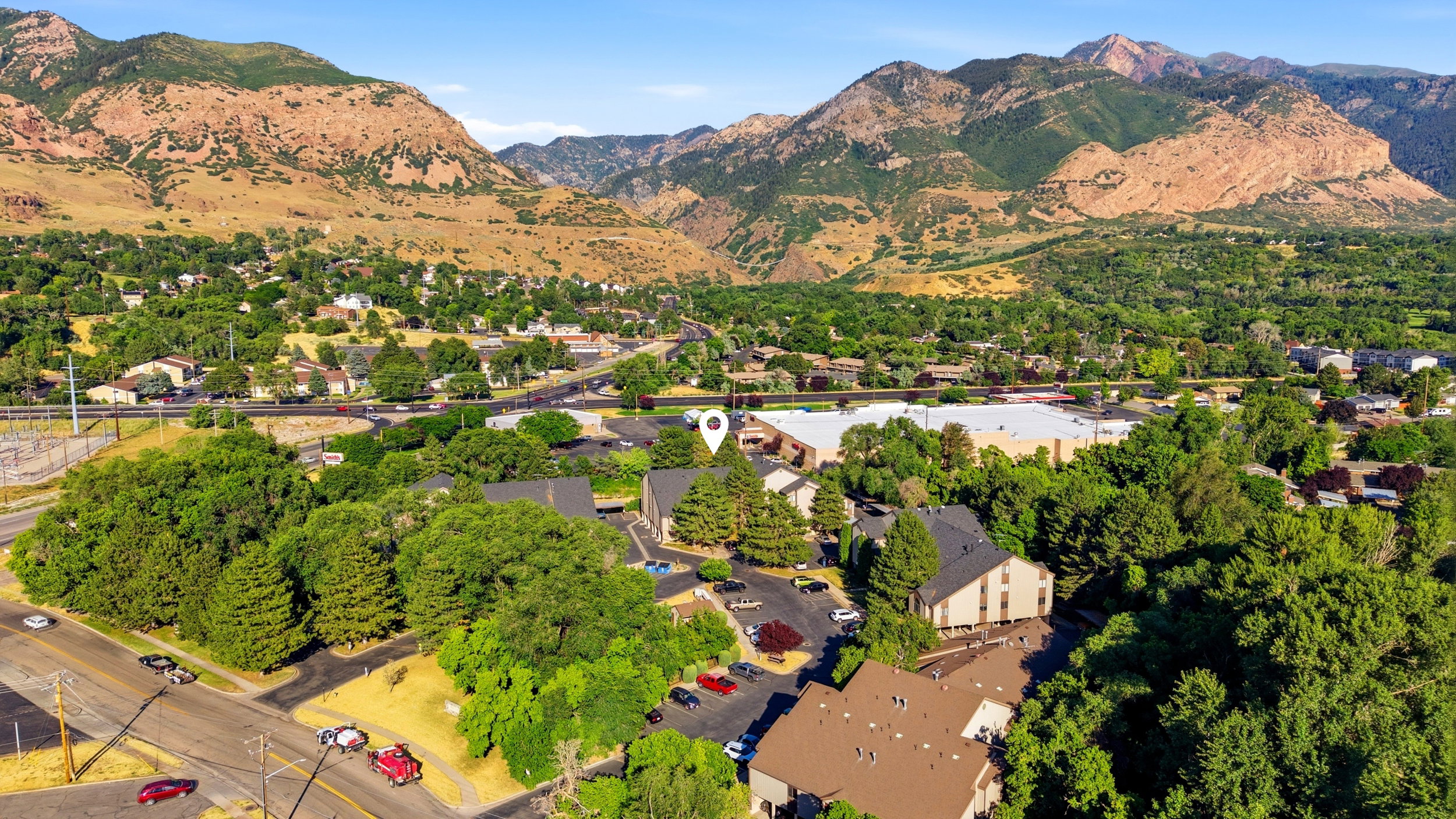 Mountainous backdrop with extensive tree coverage and visible structures, featuring multiple paved parking areas and a prominent road system