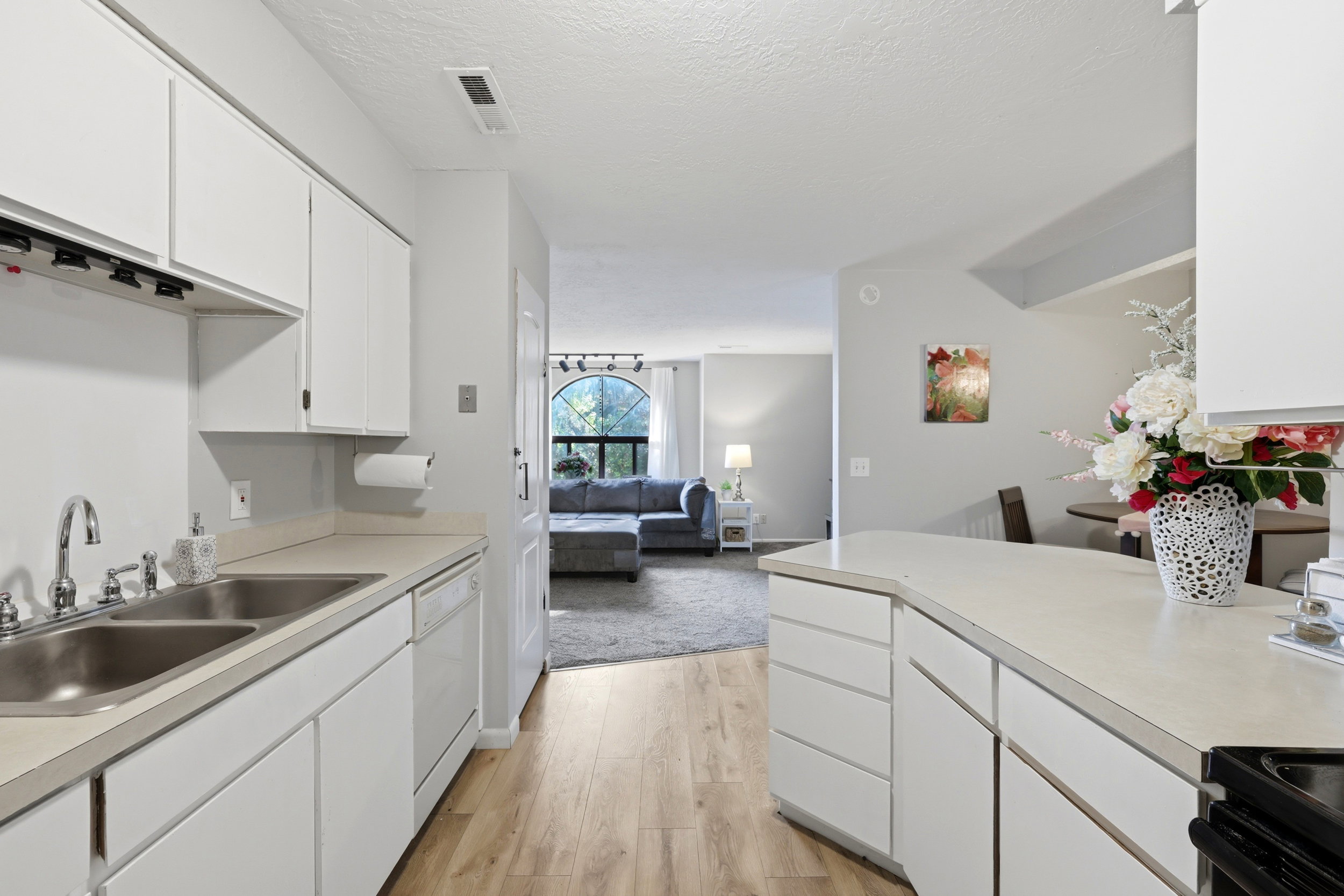 Kitchen featuring white cabinetry, light-toned countertops, a double basin stainless steel sink, and wood-finish flooring