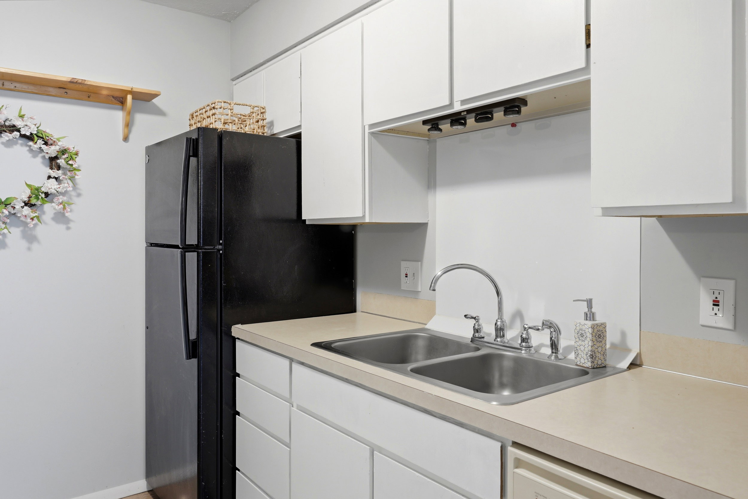 Kitchen area featuring white cabinetry, light-toned countertops, and a dual-basin stainless steel sink with a chrome faucet
