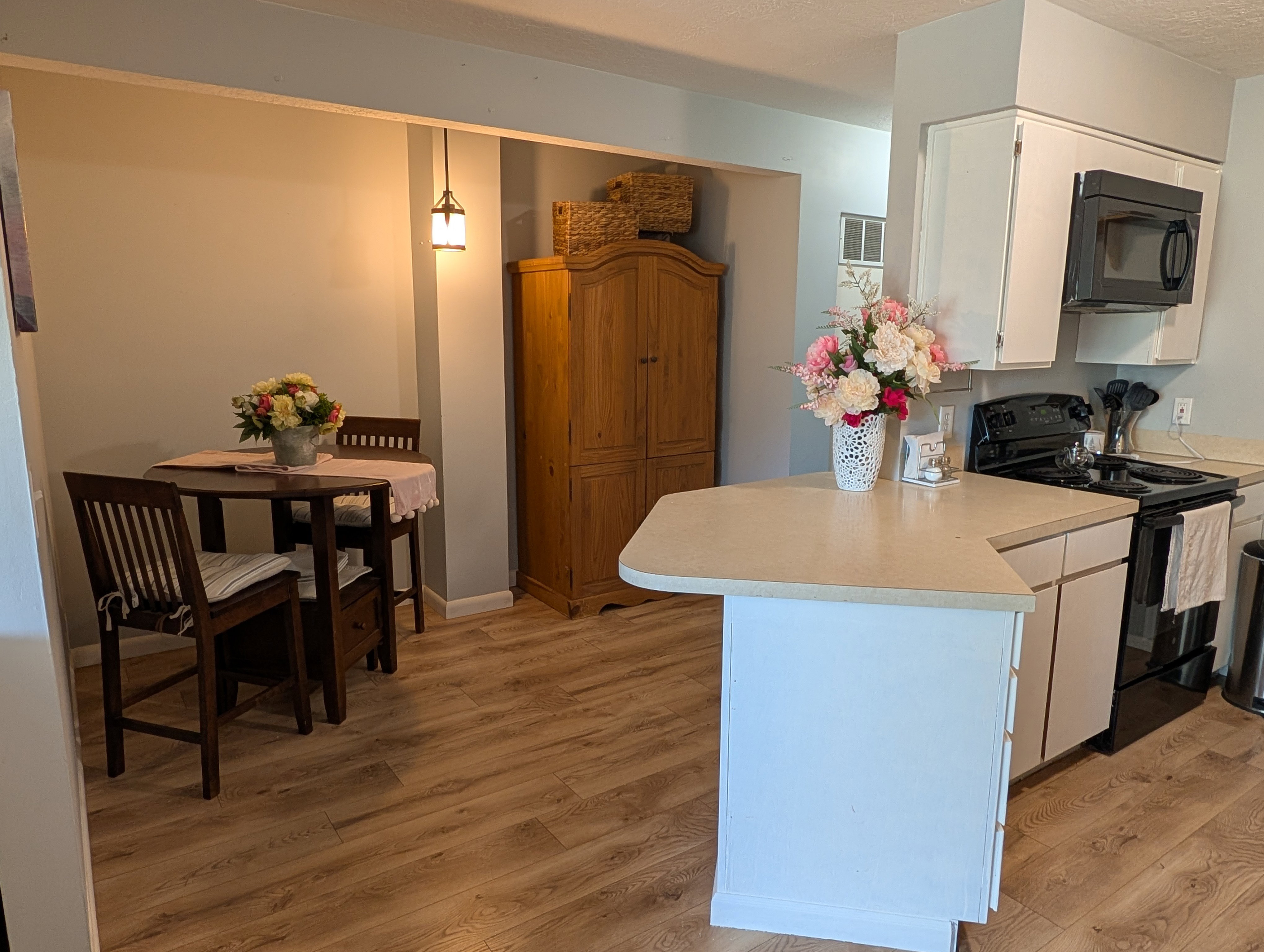 Kitchen area featuring white cabinetry, black appliances, a peninsula with a light-toned countertop, and wood-finish flooring extending into the dining area