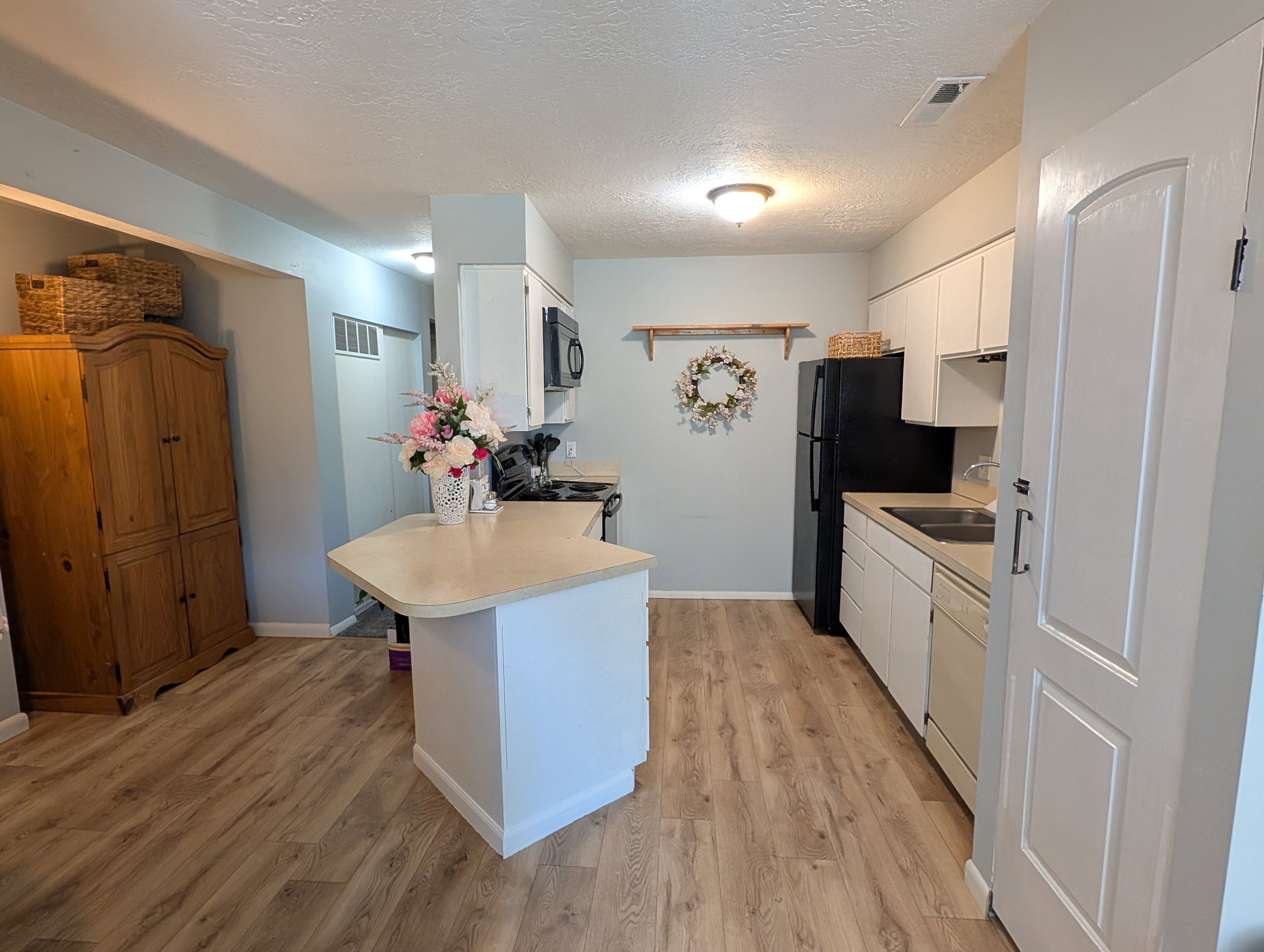 Open-concept kitchen featuring wood-finish flooring, white cabinetry, a built-in microwave, and a breakfast bar with a light-toned countertop
