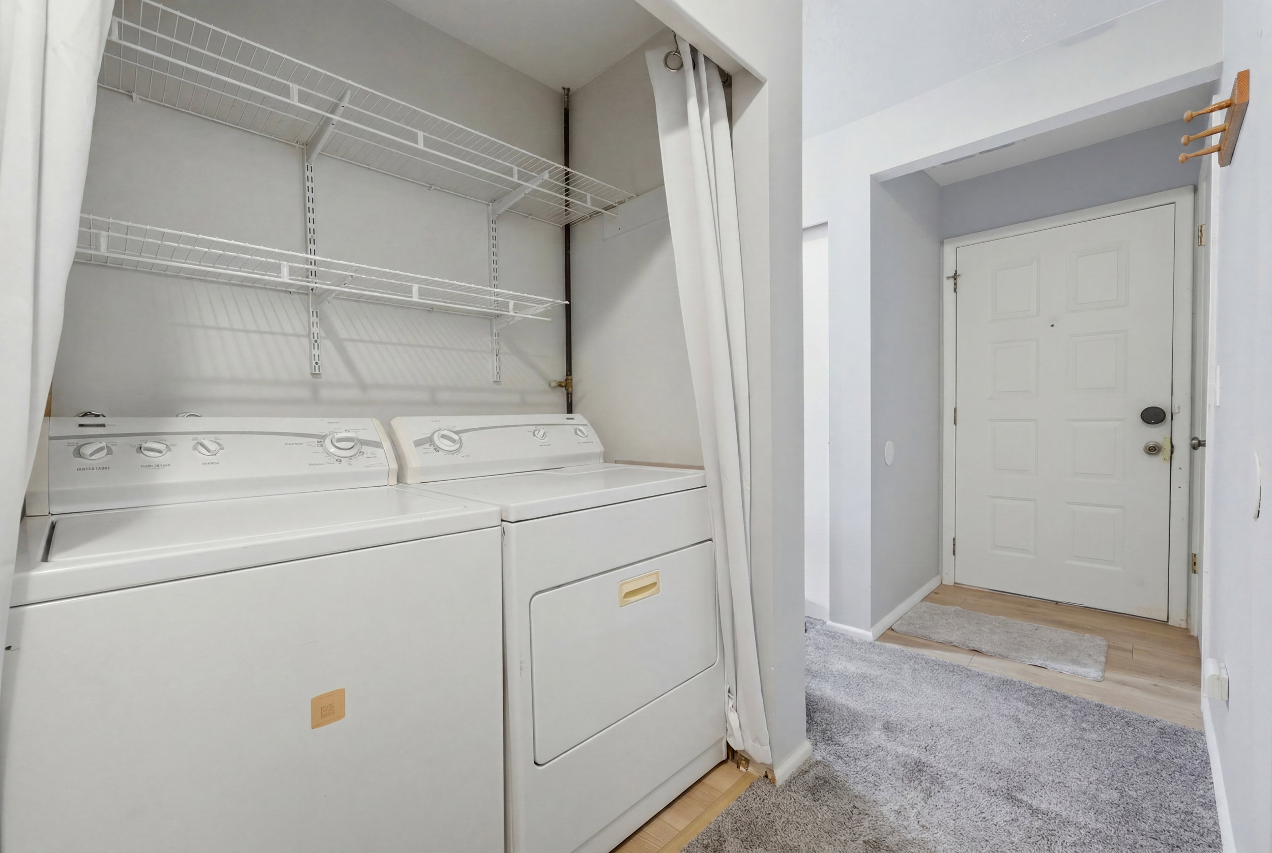 Dedicated laundry area featuring a washer and dryer, integrated shelving, and a privacy curtain