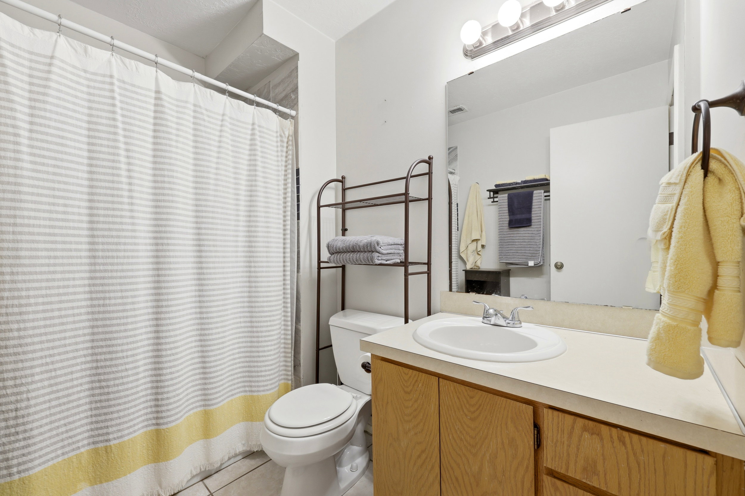 Bathroom featuring a built-in vanity with a white oval sink, light wood-finish cabinetry, and a full-width mirror with a three-bulb light fixture
