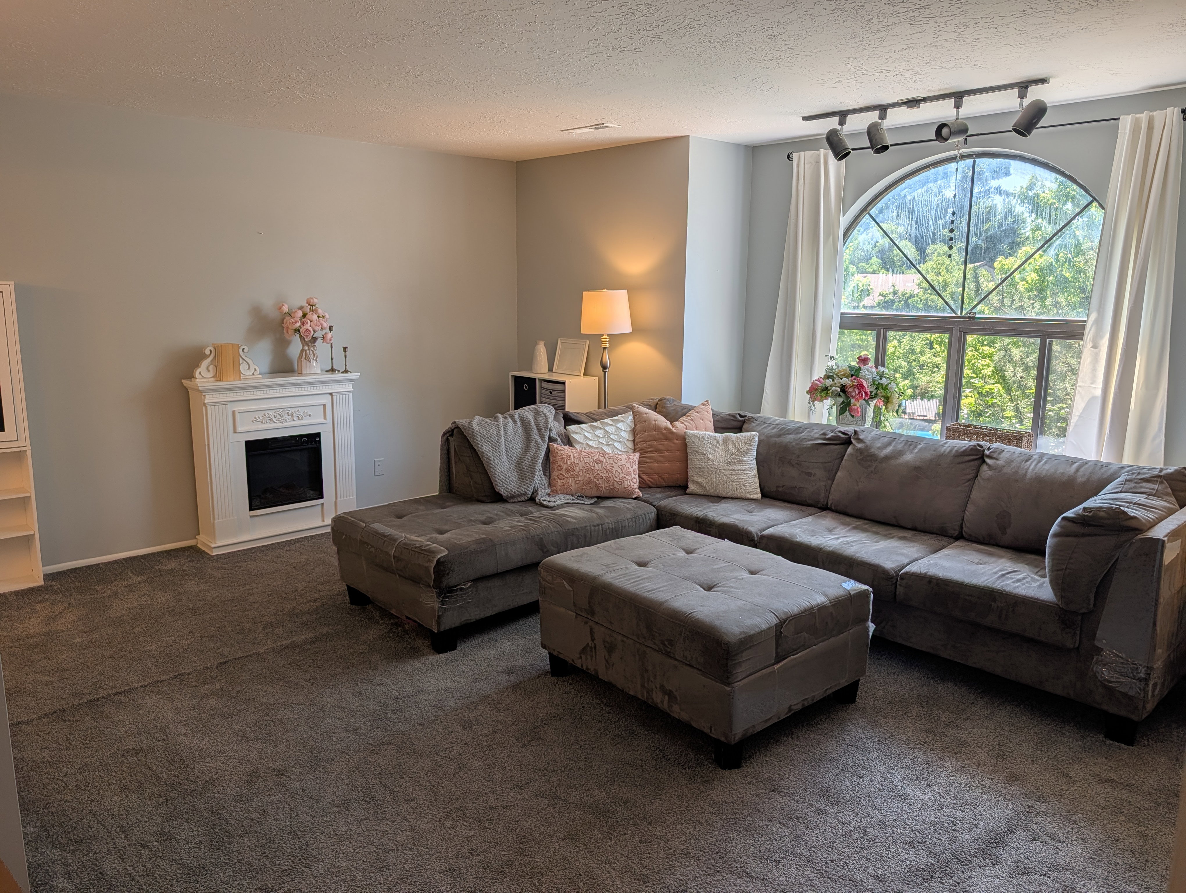 Bright living space featuring an arched window, track lighting, and a white decorative fireplace surround