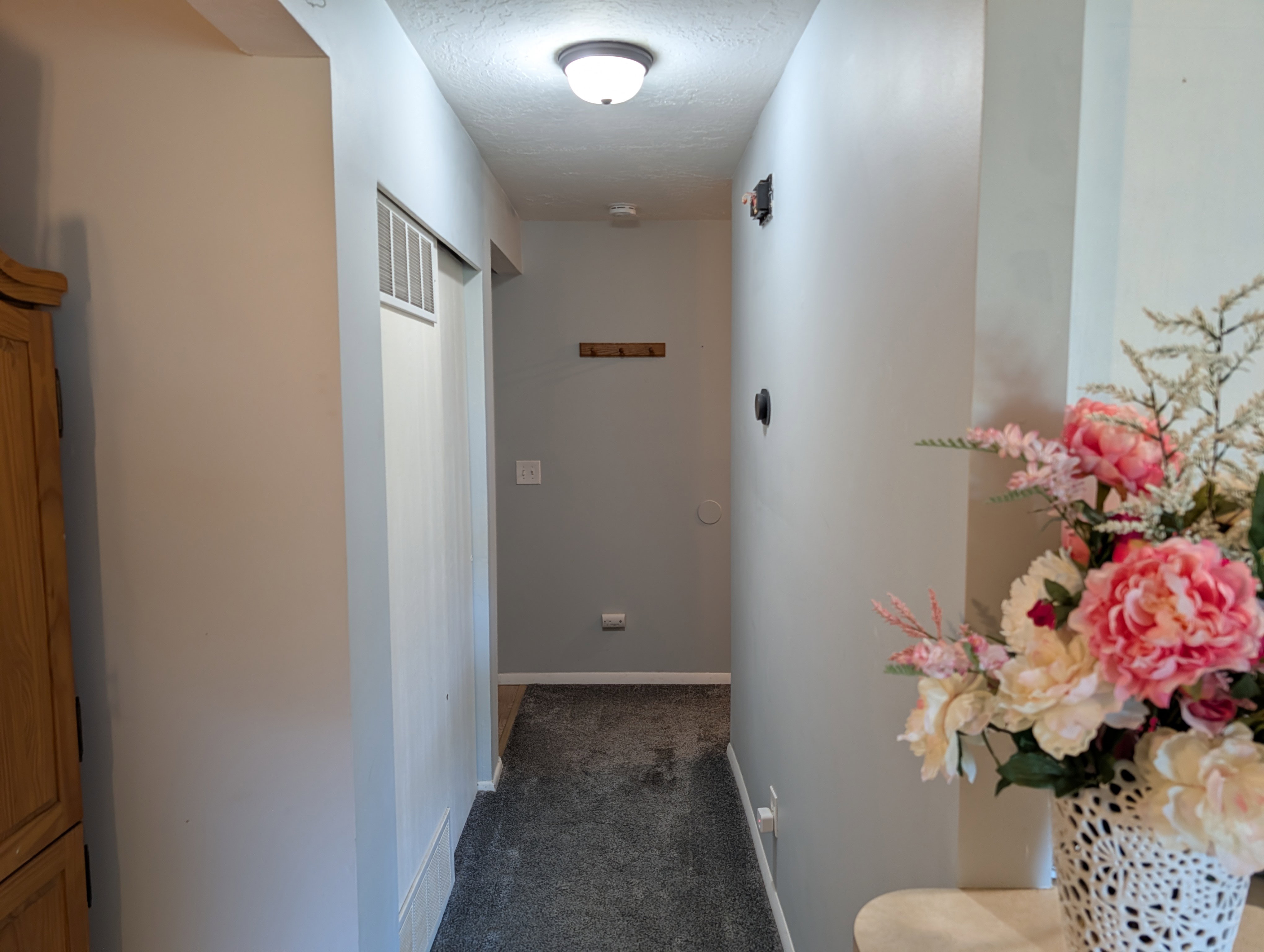 Hallway featuring neutral-toned walls, ceiling-mounted lighting, and dark grey carpeting