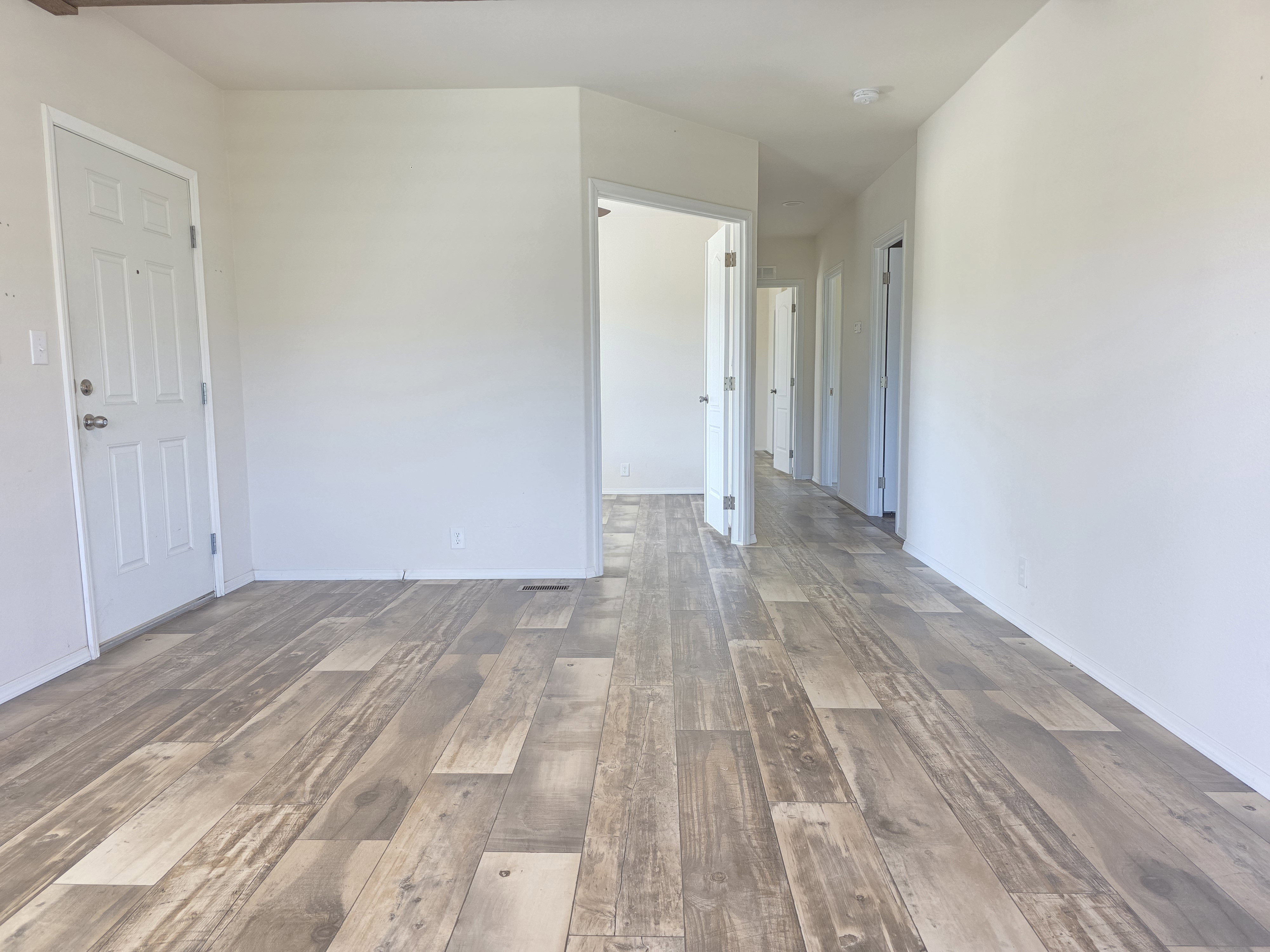 Spacious interior featuring wide plank wood-finish flooring, white painted walls, and a visible wood beam accent