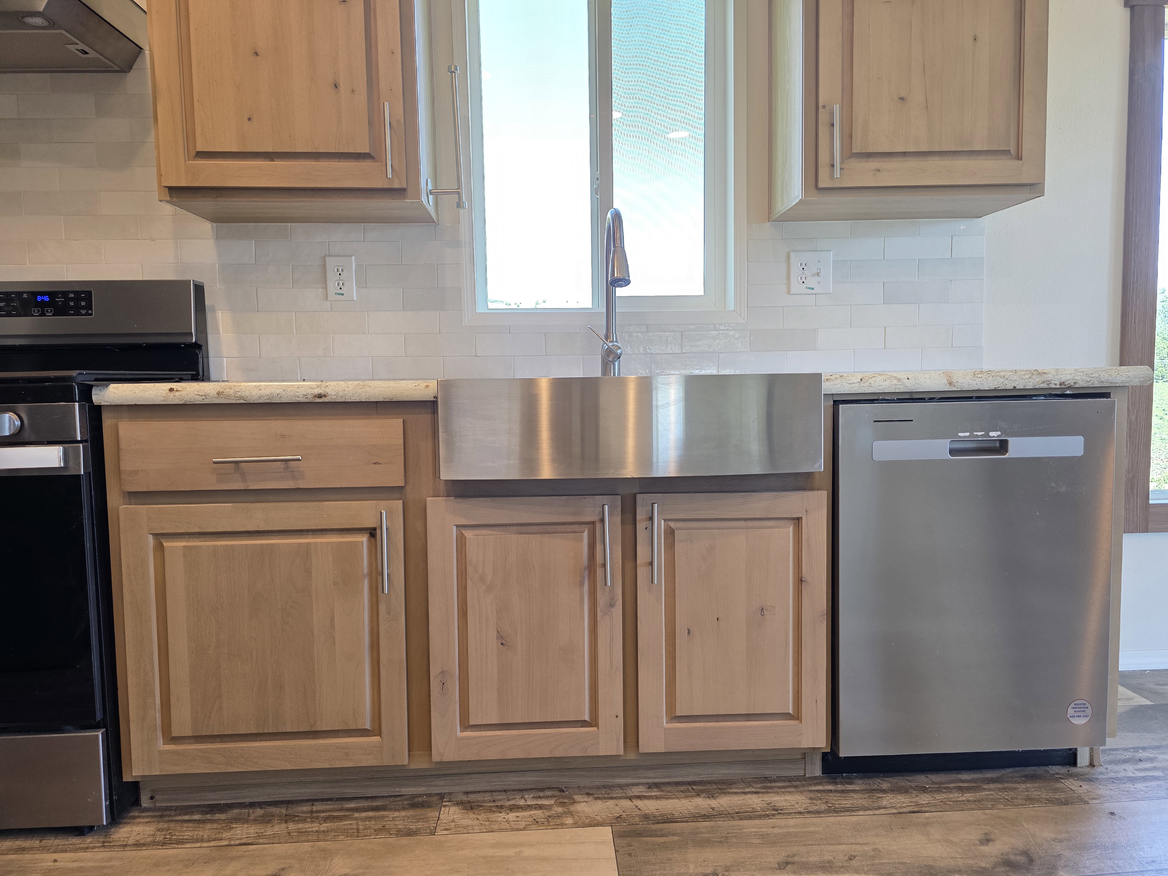 Kitchen featuring light wood cabinetry, stainless steel apron-front sink, light-toned countertops, and subway tile backsplash
