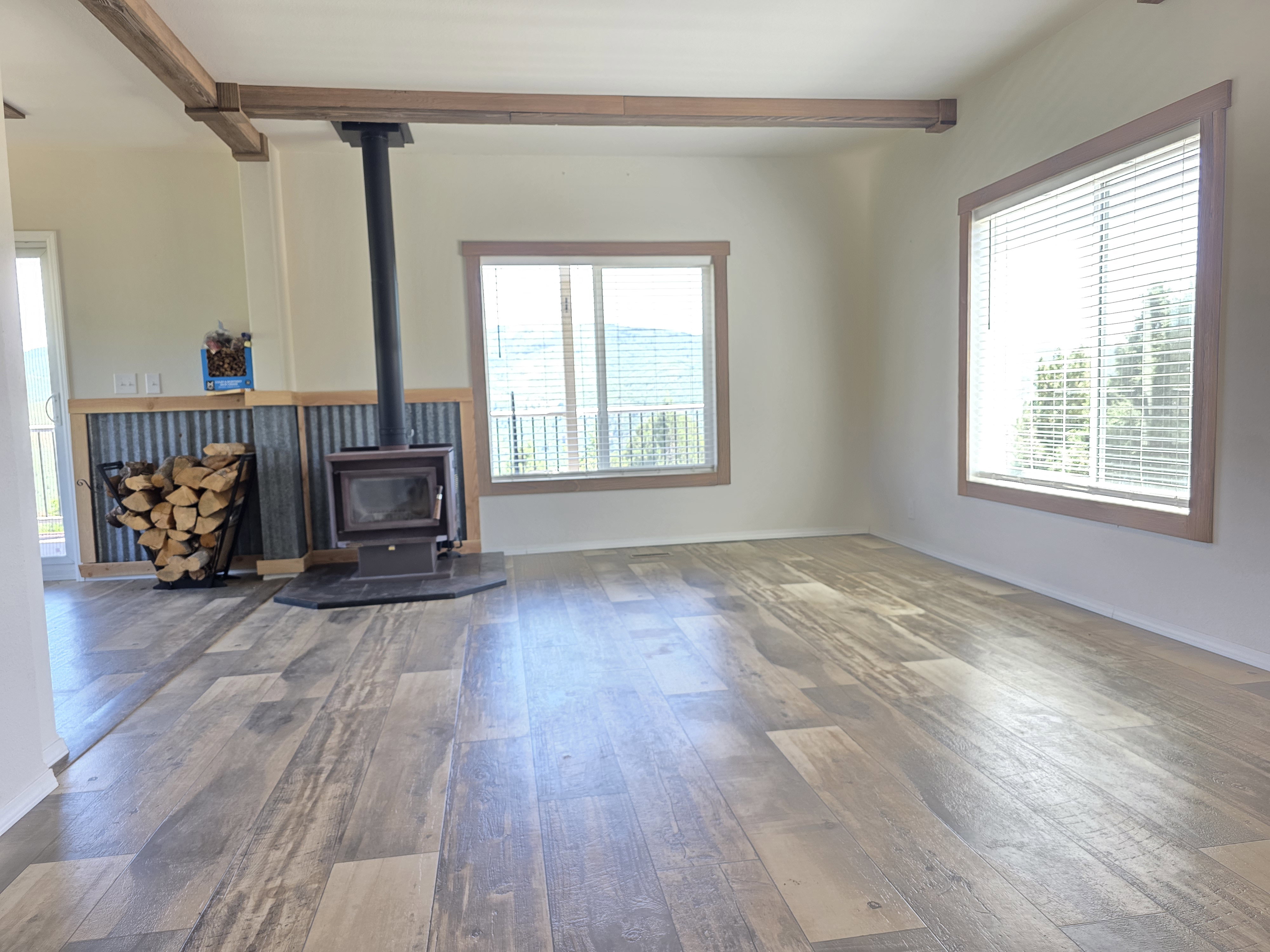 Spacious room featuring wood-finish flooring, a freestanding wood-burning stove with a stone-finish hearth, and architectural ceiling beams