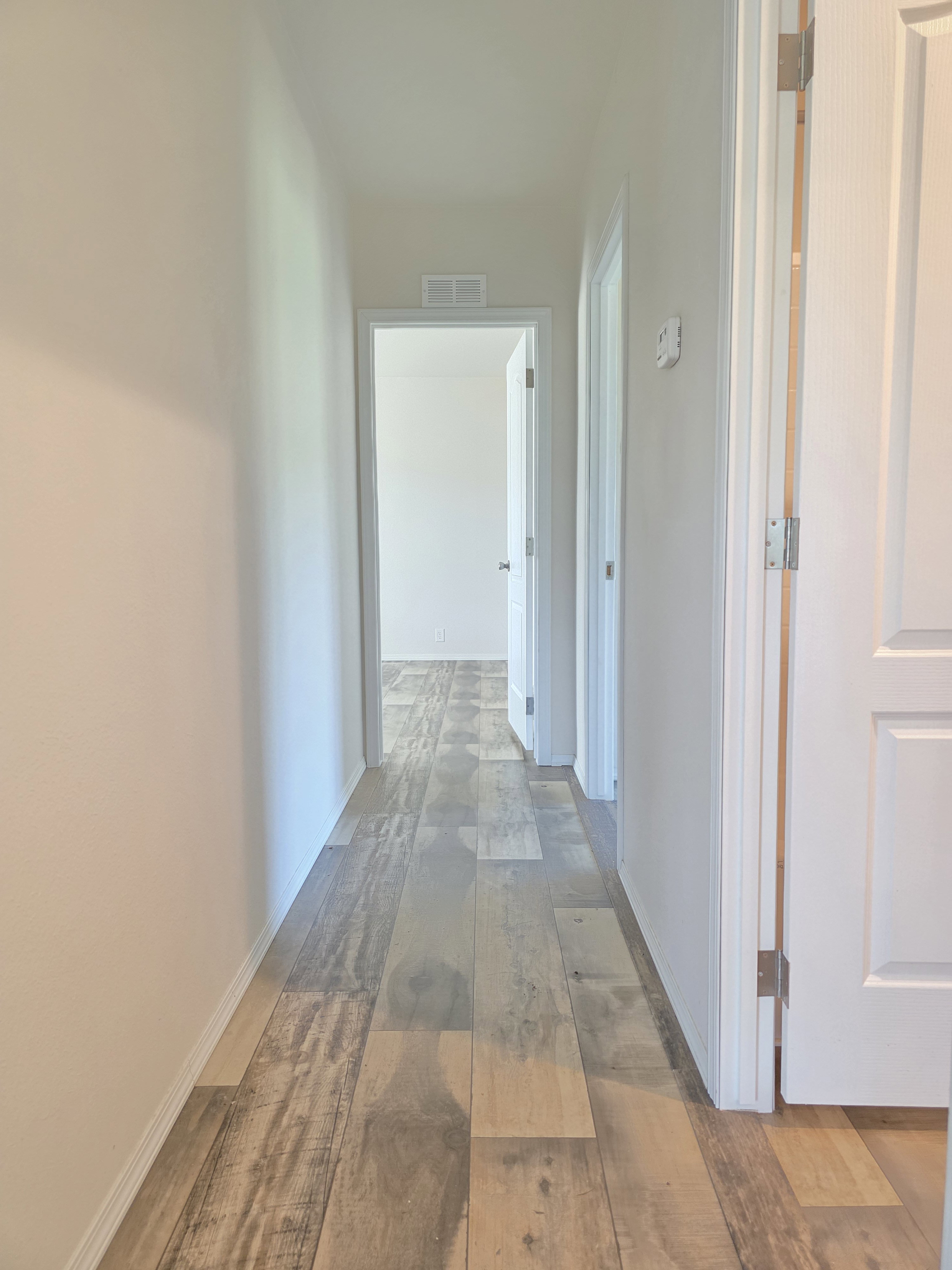 Interior hallway featuring wood-finish flooring, white baseboards, and light-toned walls
