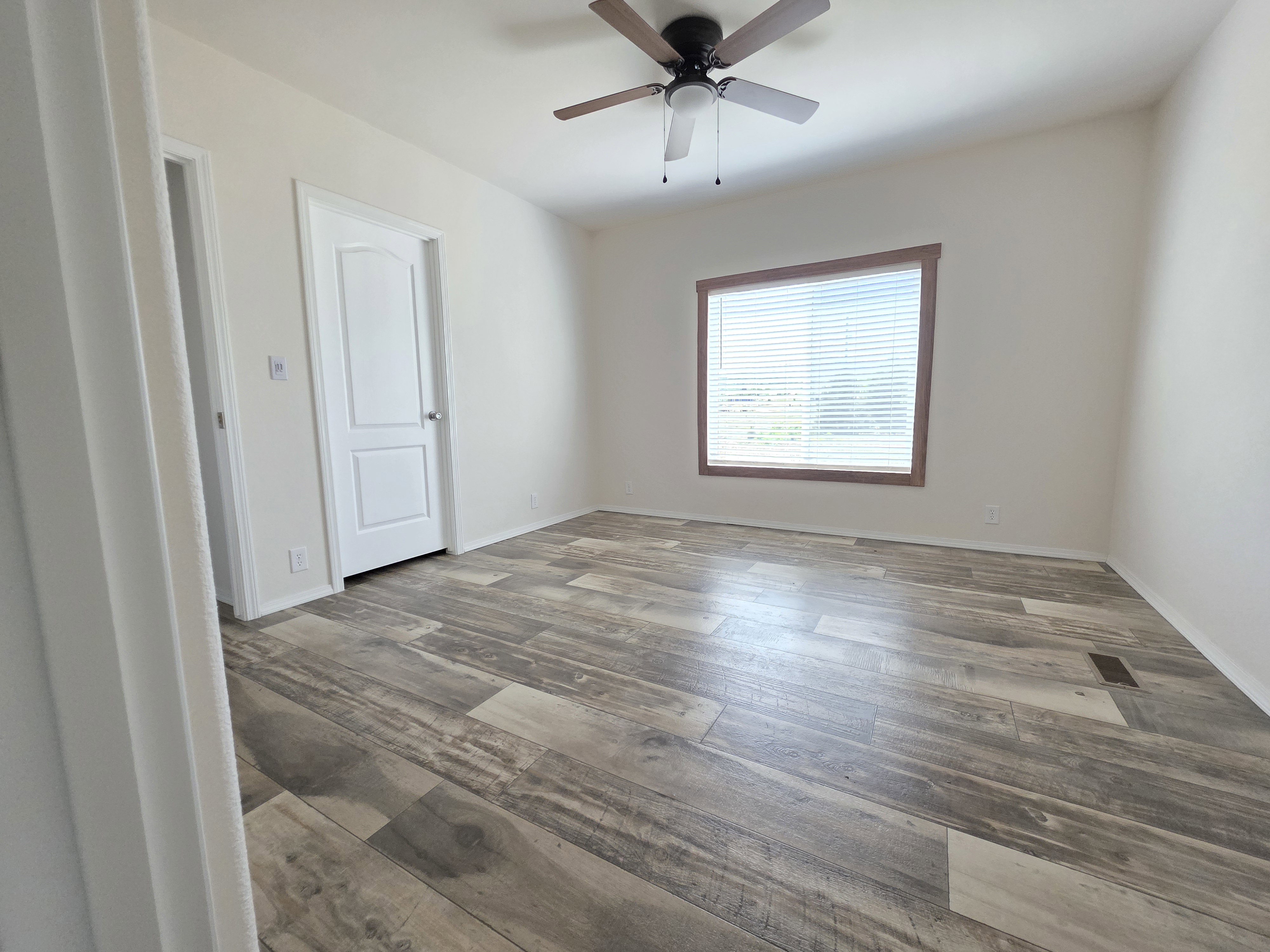 Room featuring wide plank wood-finish flooring, a ceiling fan with light fixture, and a window with blinds