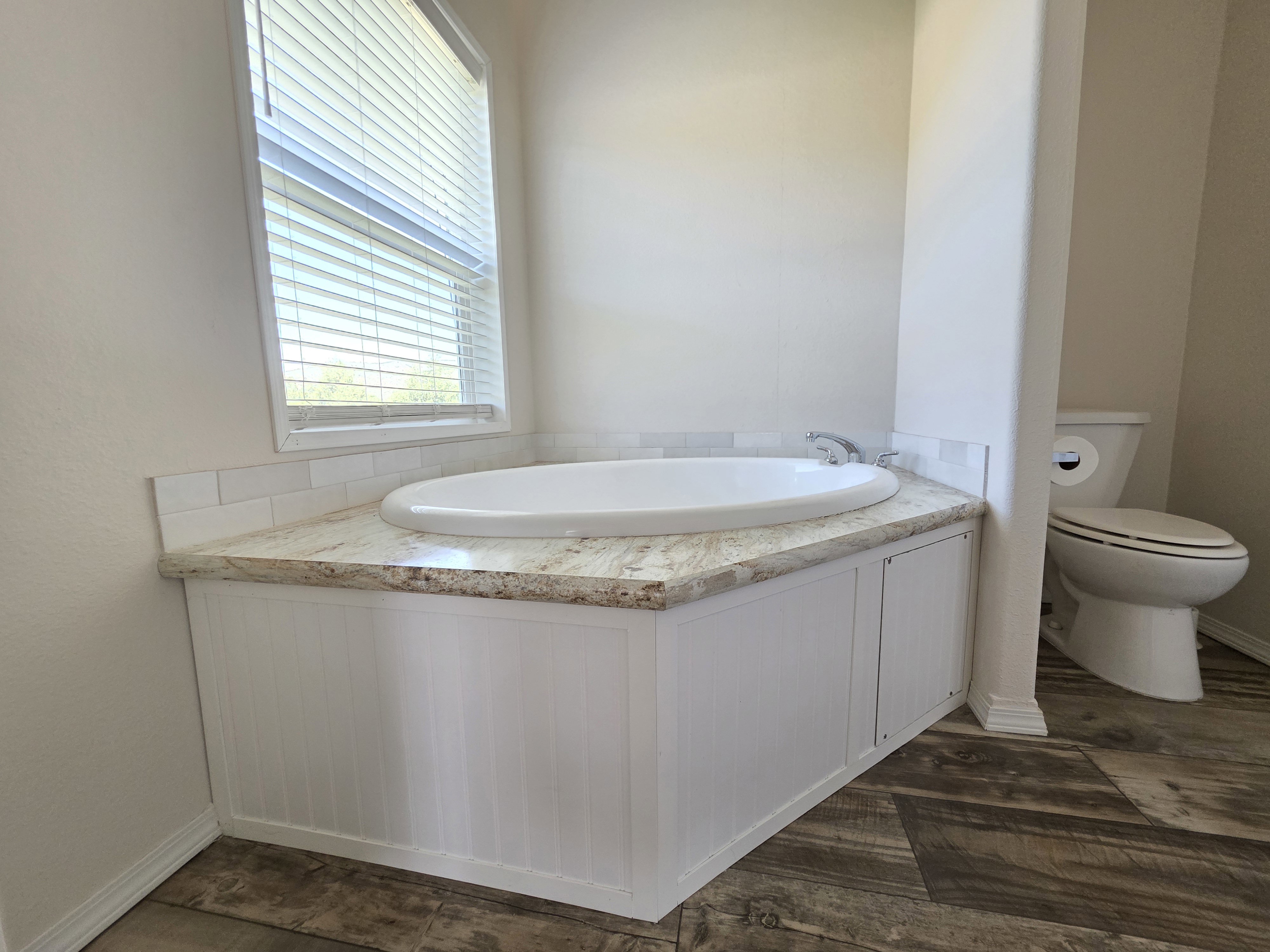 Corner soaking tub with a tiled surround, integrated into a granite-look countertop
