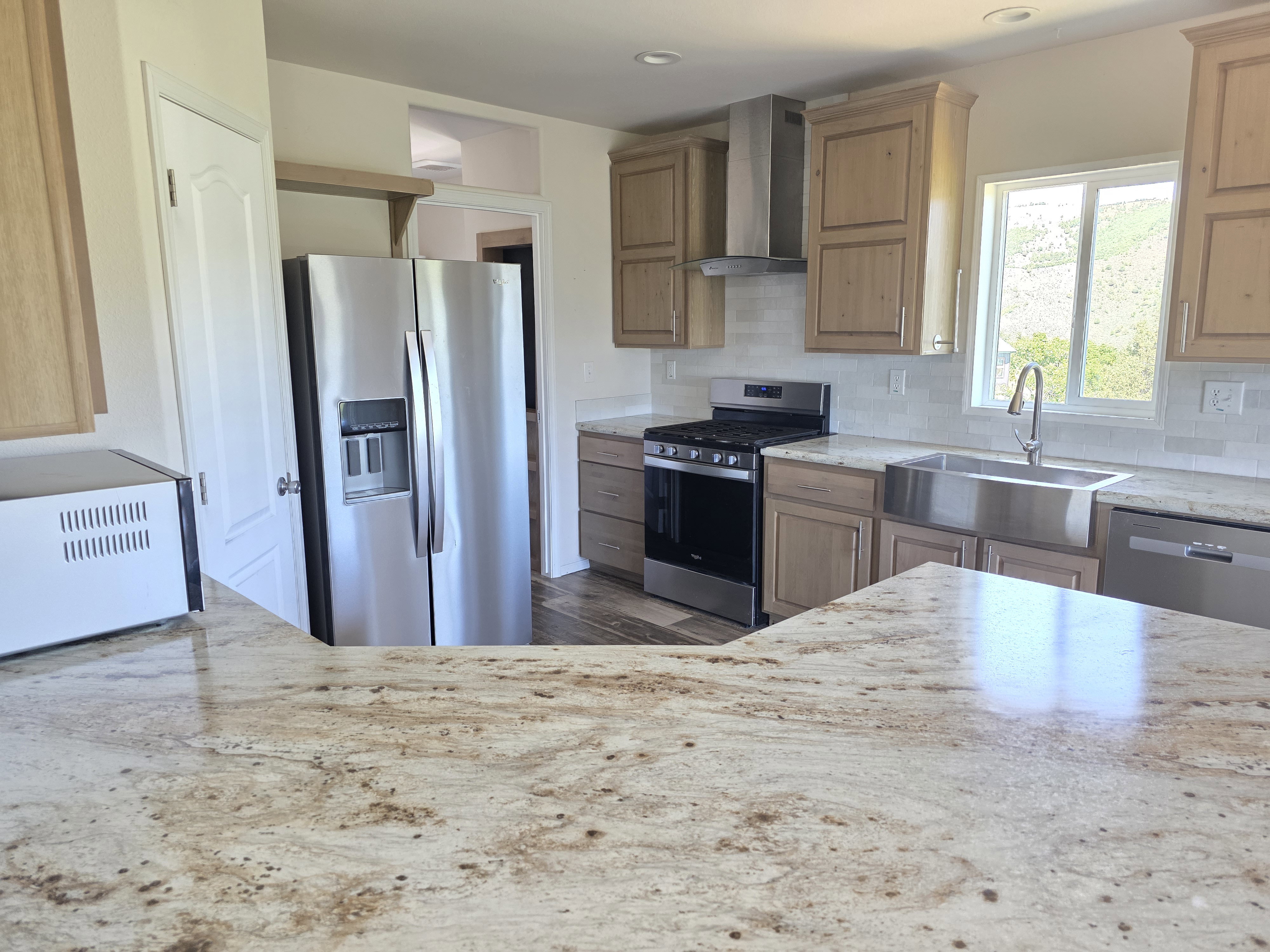 Spacious kitchen featuring granite countertops, wood-finish cabinetry, stainless steel appliances, a farmhouse sink, and a tile backsplash