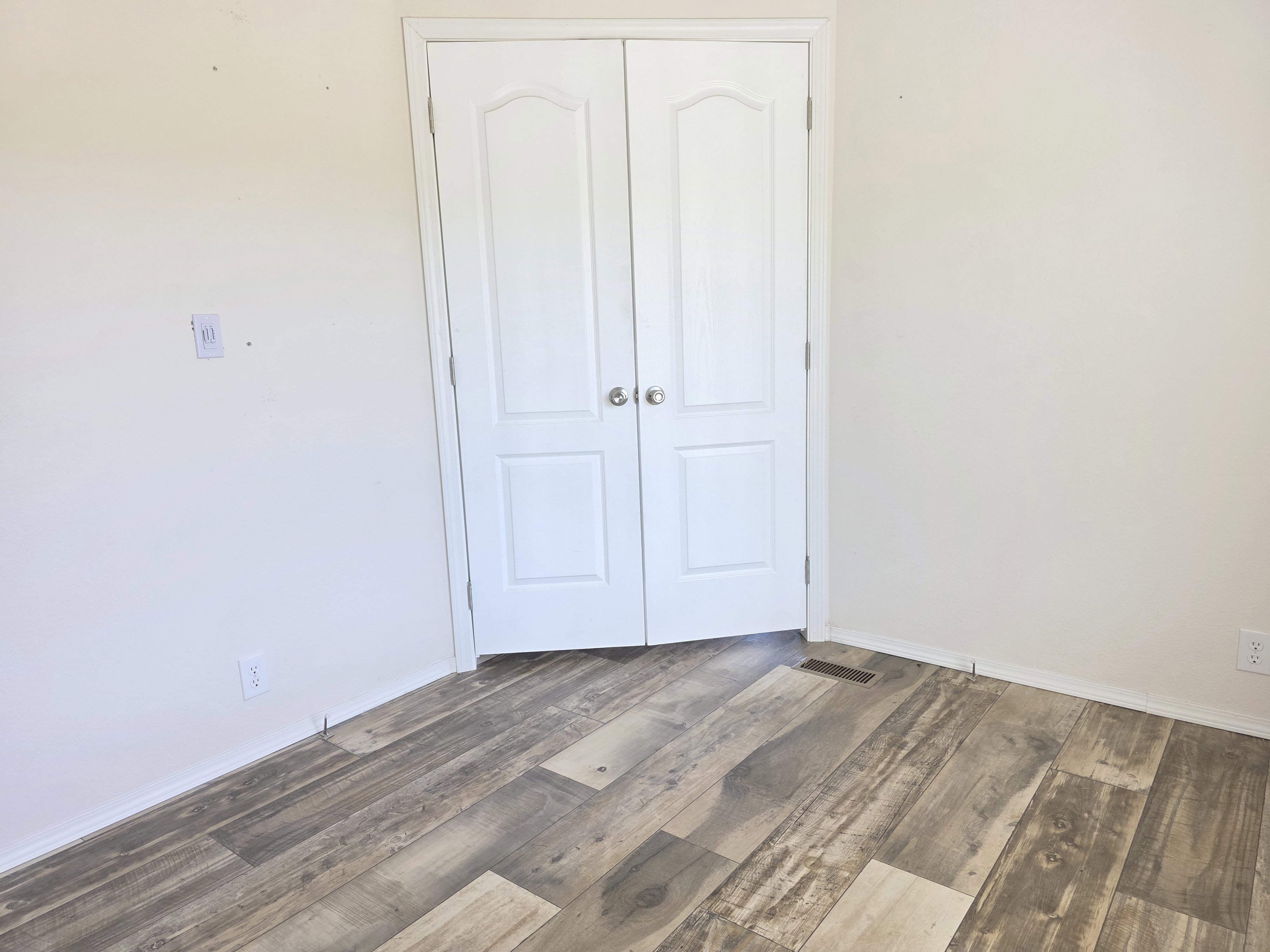 White bi-fold doors open to reveal a closet space, complemented by wide plank wood-finish flooring