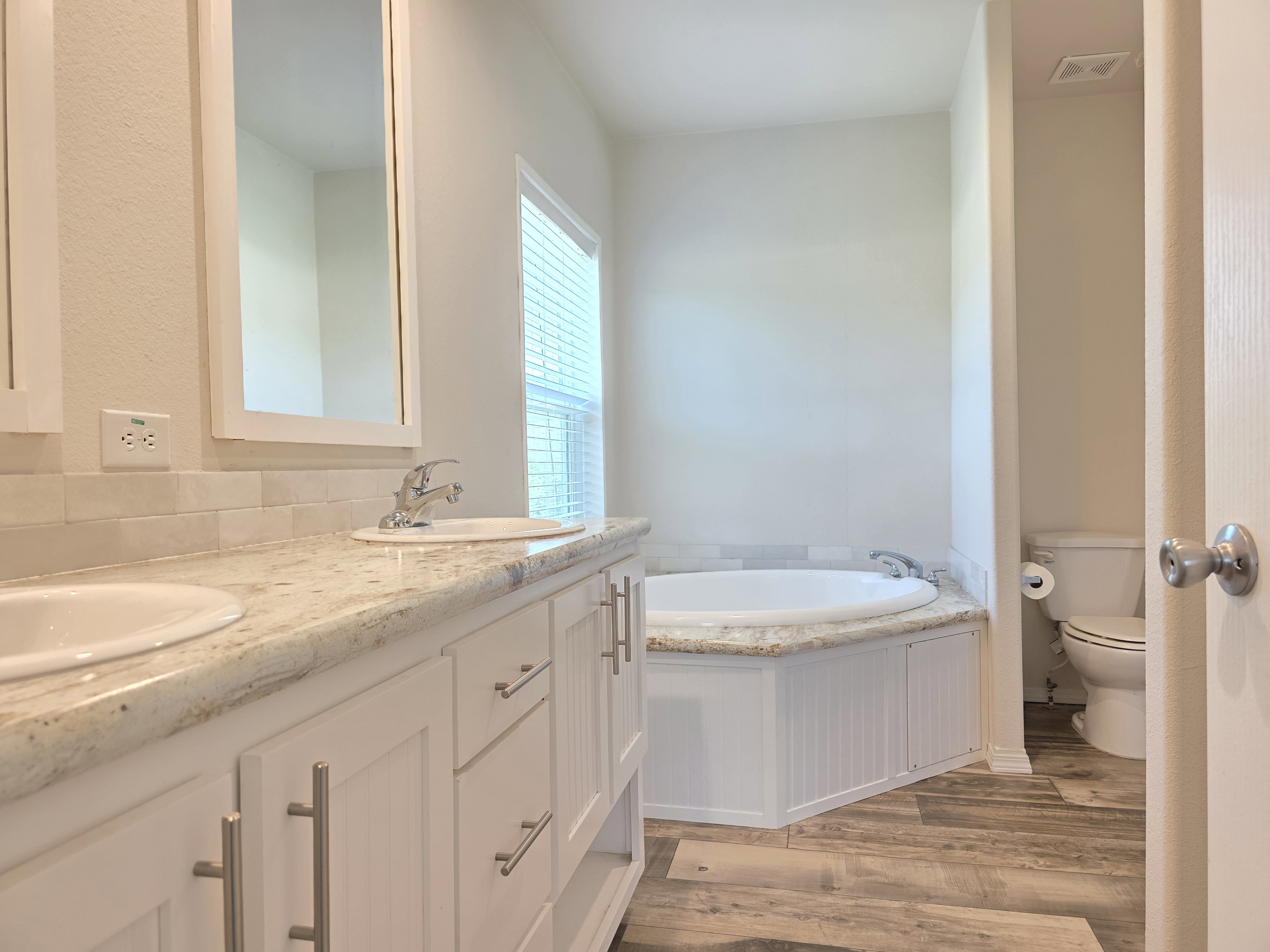 Double vanity with undermount sinks, light-toned countertop, and white cabinetry featuring brushed nickel hardware