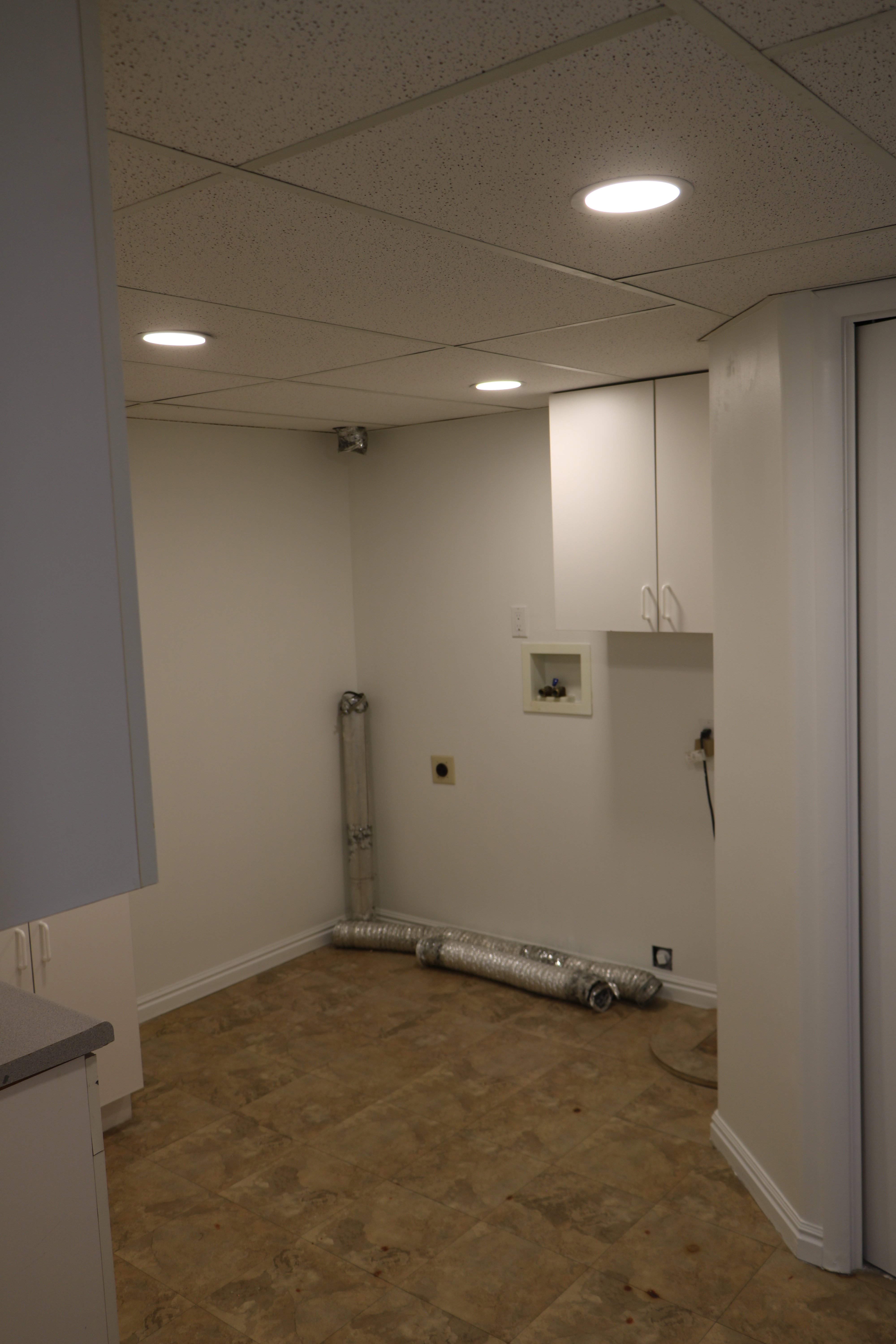 Dedicated laundry room featuring a drop ceiling with recessed lighting, white cabinetry, a utility sink, and durable vinyl flooring