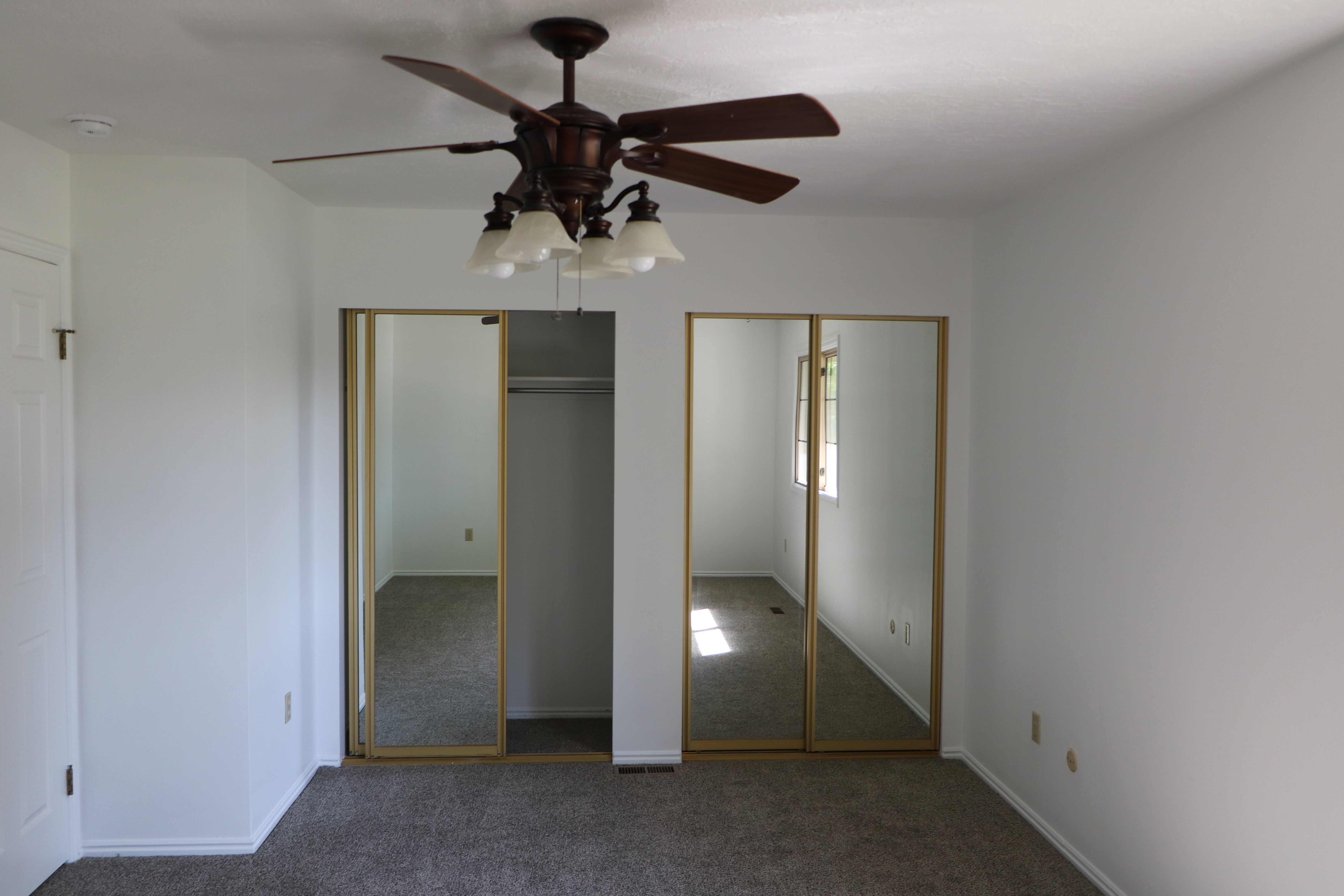 Bedroom featuring a ceiling fan with integrated lighting, carpet flooring, a white paneled door, and two mirrored sliding closet doors with gold-finish frames