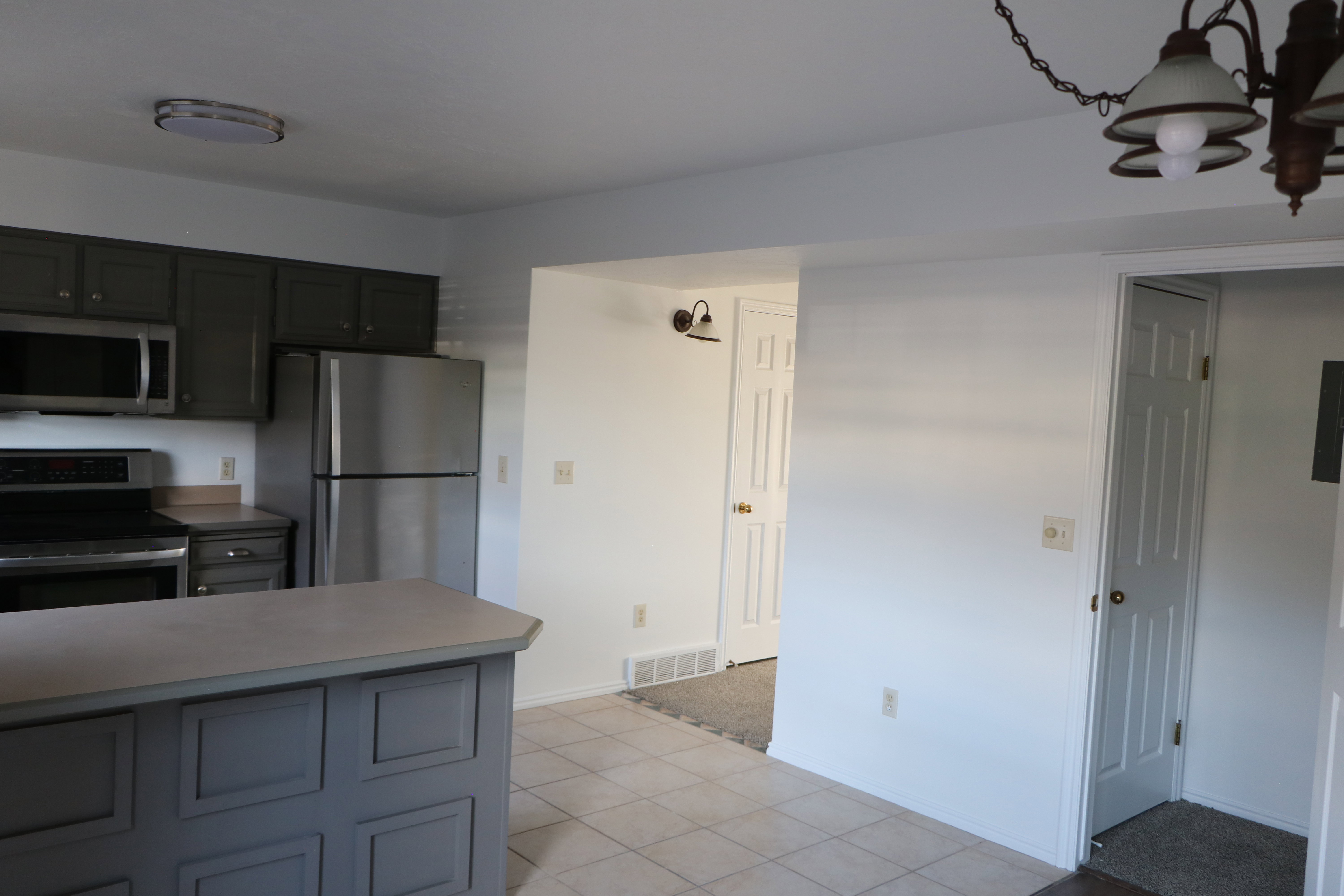 Kitchen featuring stainless steel appliances, grey cabinetry, a functional island with a light-toned countertop, and light-toned tile flooring