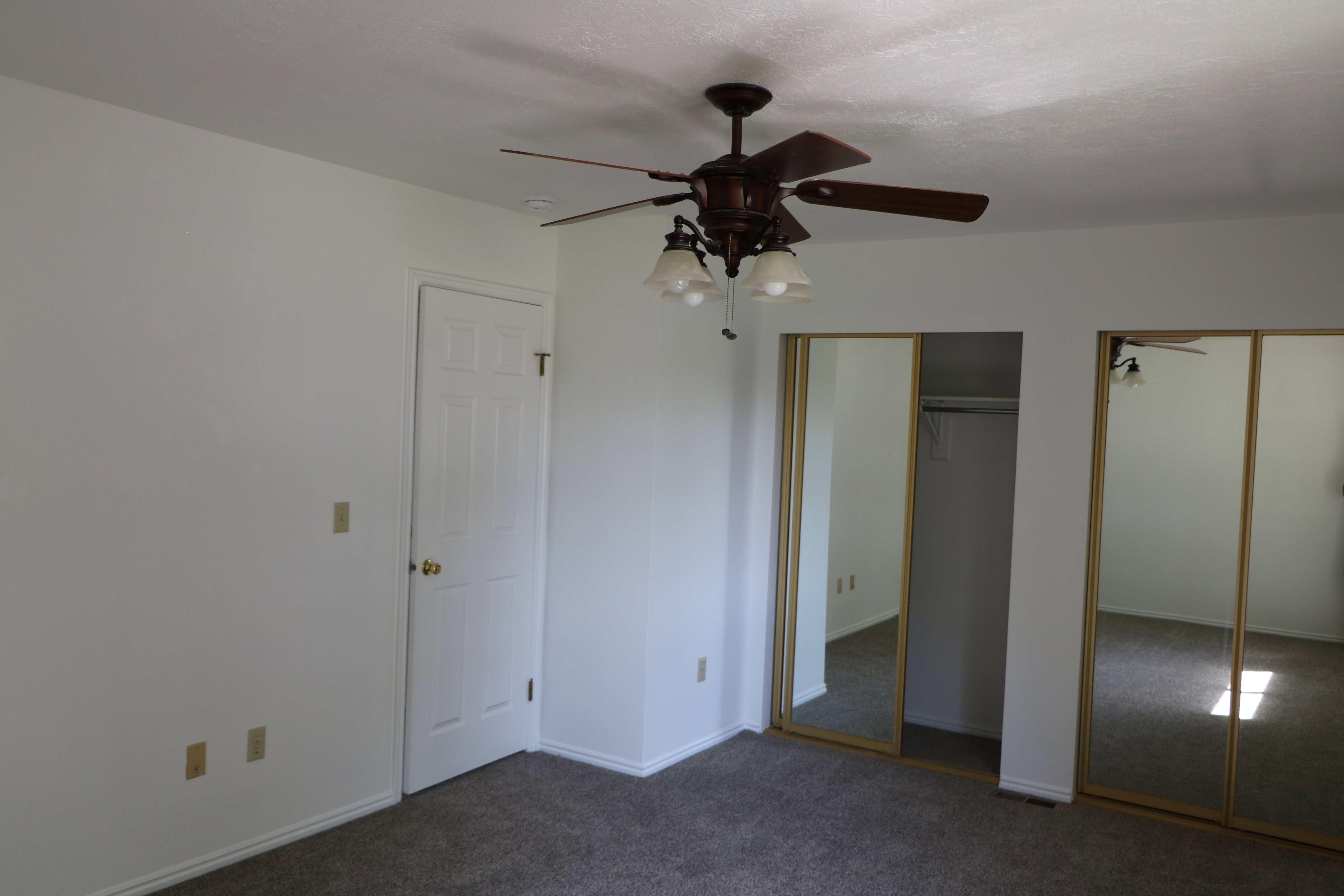 Room featuring a ceiling fan with integrated lighting, textured white walls, and a multi-panel door with brass hardware